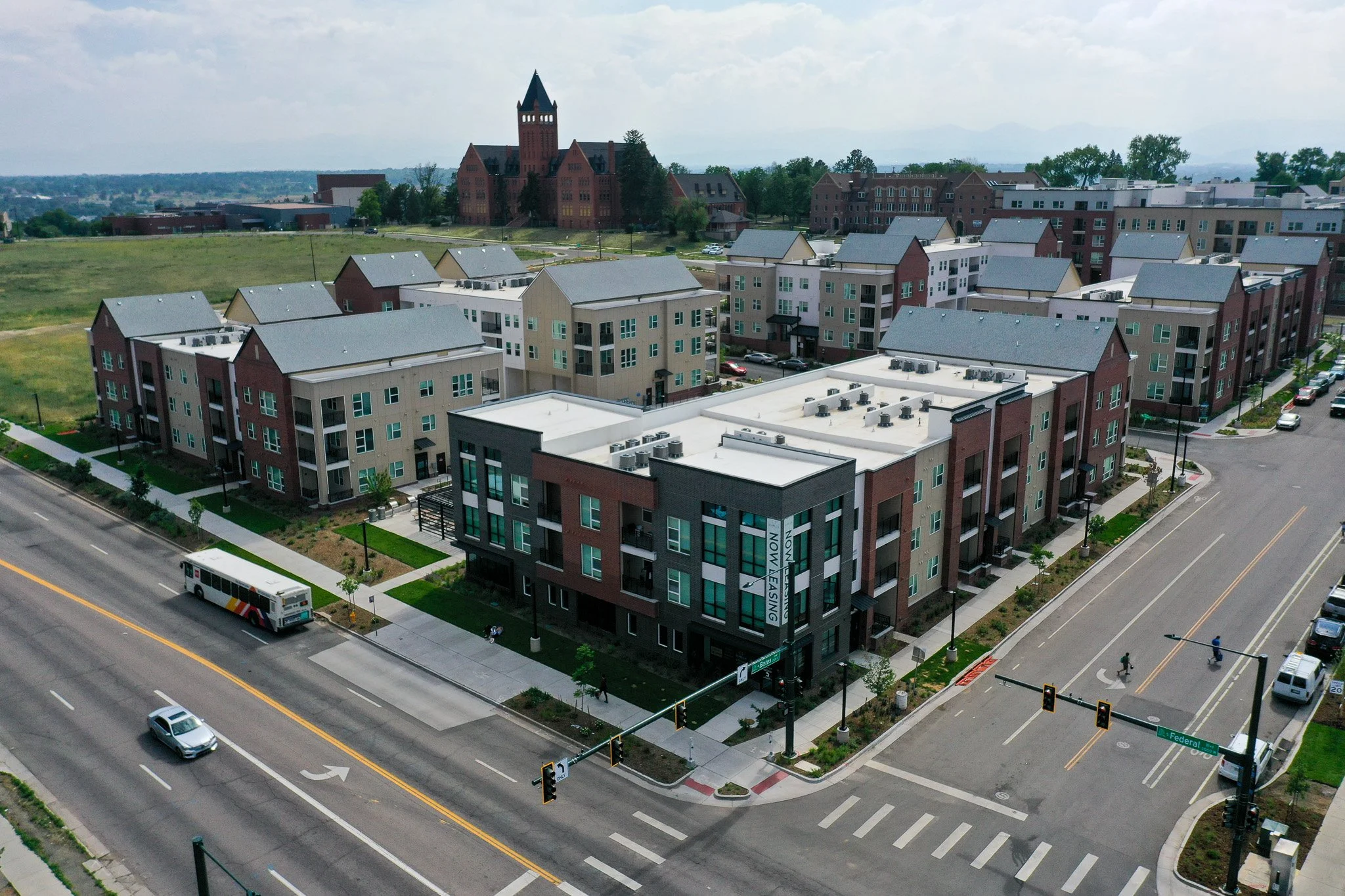 Aerial view of a modern apartment complex with multiple buildings, a bus, cars, and a street intersection.