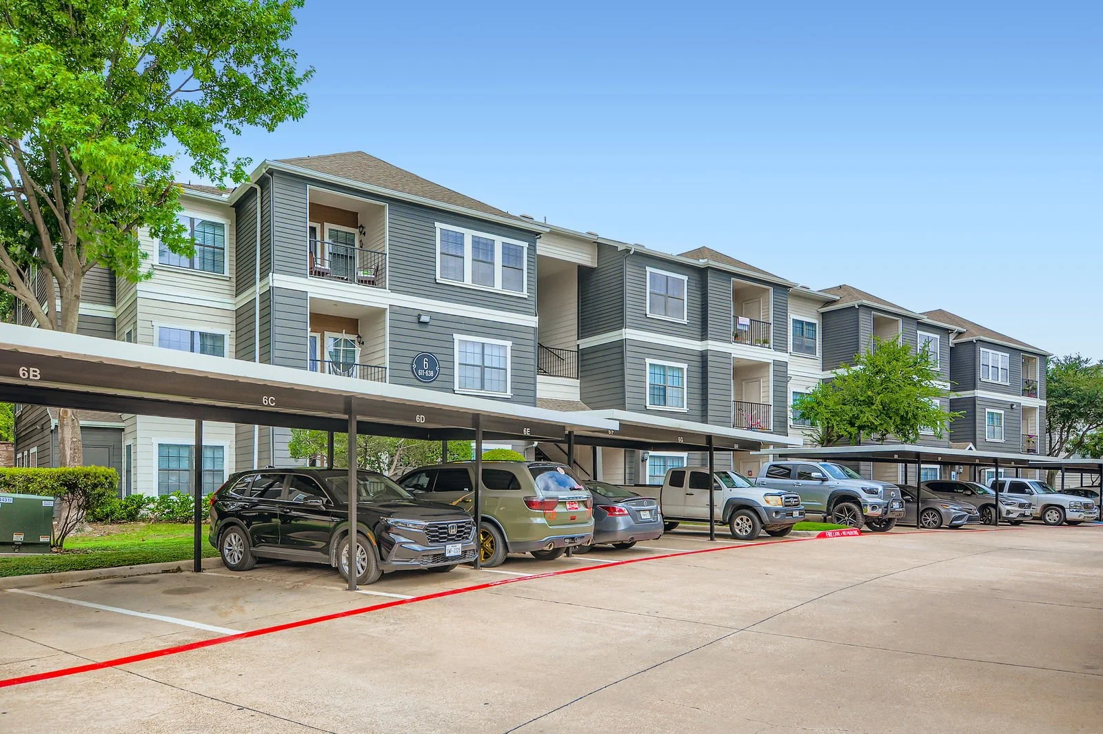 Multi-story apartment building with balconies and a covered parking lot in the foreground, with several parked cars.