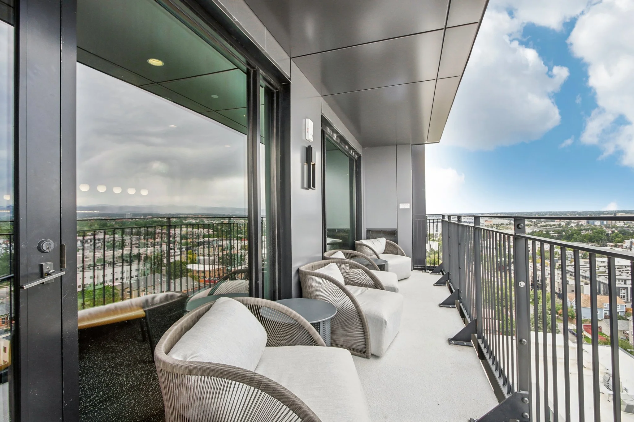 Luxury rooftop balcony with modern outdoor chairs and small tables, overlooking a cityscape with cloudy sky.