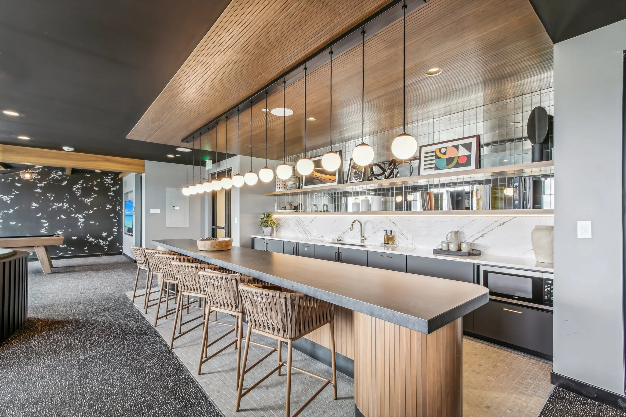Modern kitchen with a long island, pendant lights, black and gray cabinetry, open shelving, and decorative artwork.