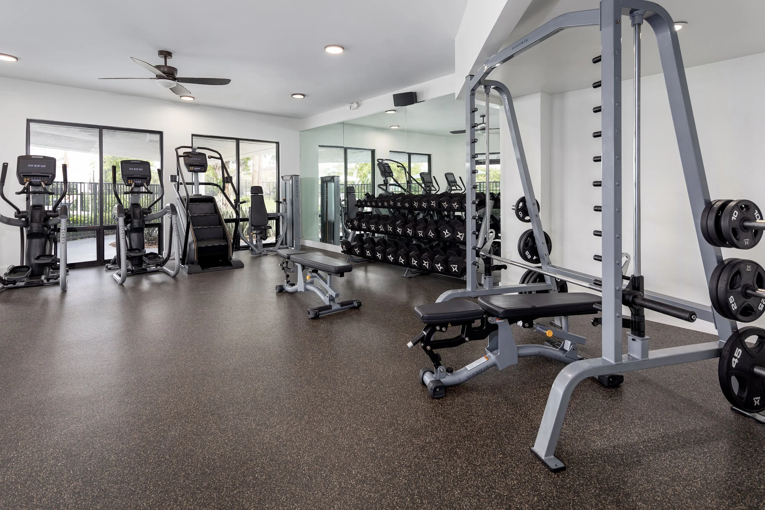 Empty modern gym with cardio machines, weight racks, and mirrors.