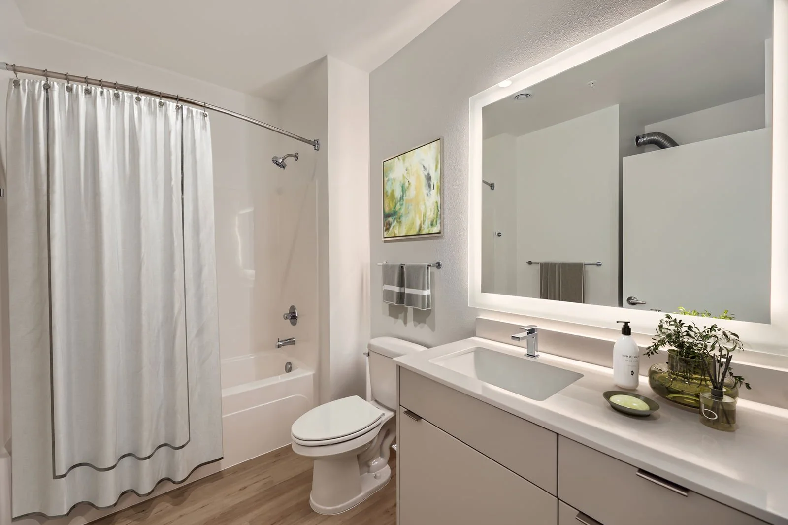 Modern bathroom with a shower and bathtub, a white toilet, a vanity with a sink, large framed mirror, decorative plants, and a towel on a rack.