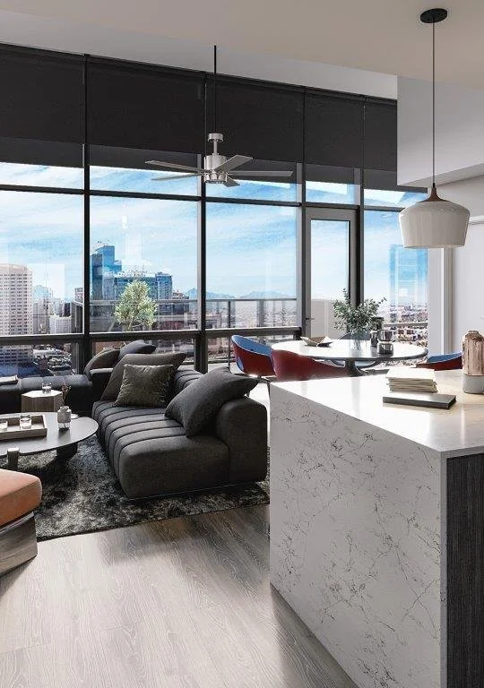 Modern living room with floor-to-ceiling windows and city view, a dark sofa with pillows, a round coffee table with candles, a marble kitchen island with books, and a dining area with red chairs and plants.