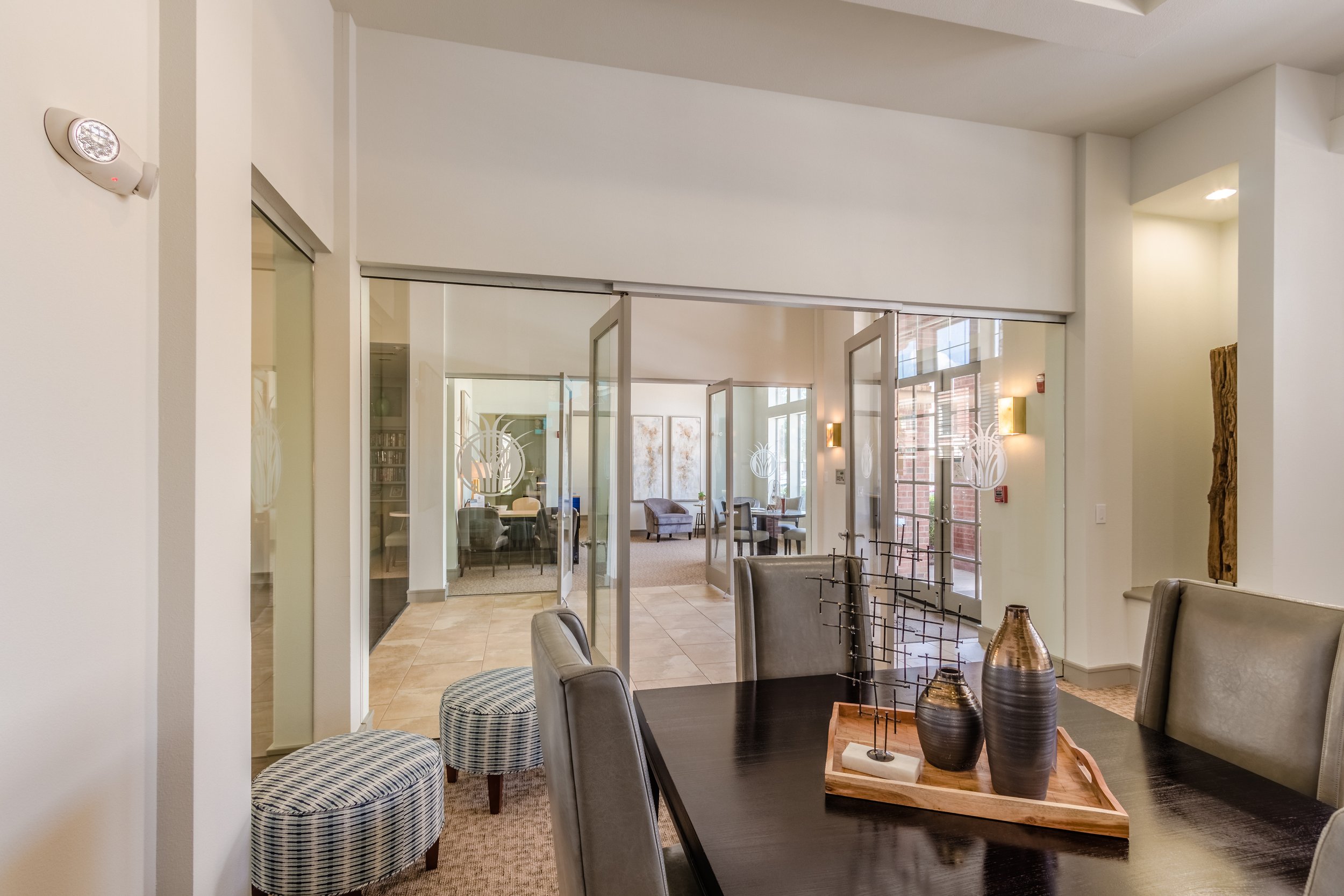 Interior view of a modern lounge area with glass doors, chairs, and tables with decorative vases.