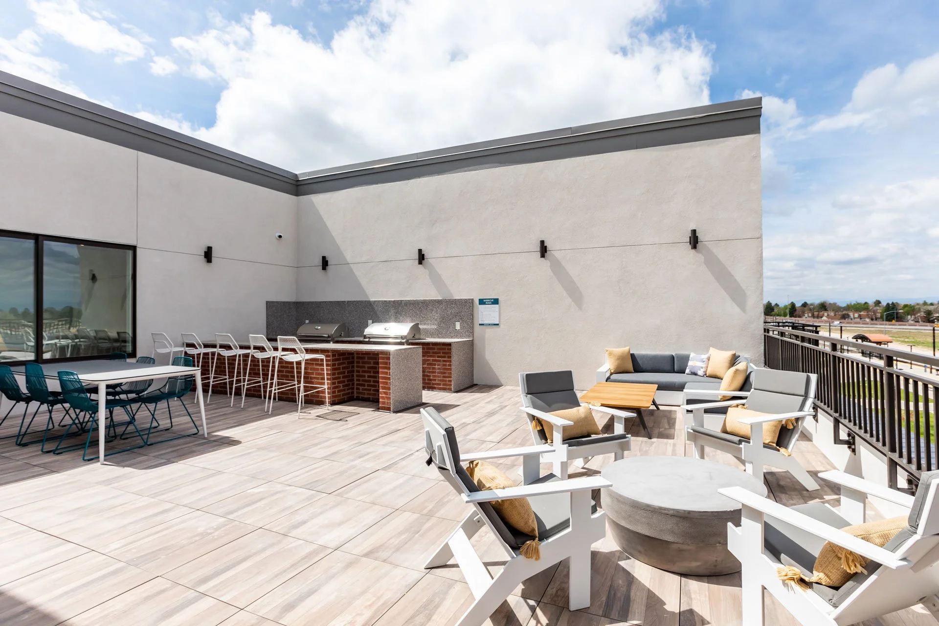 Outdoor rooftop patio with seating area, a barbecue grill, and a sky with clouds.