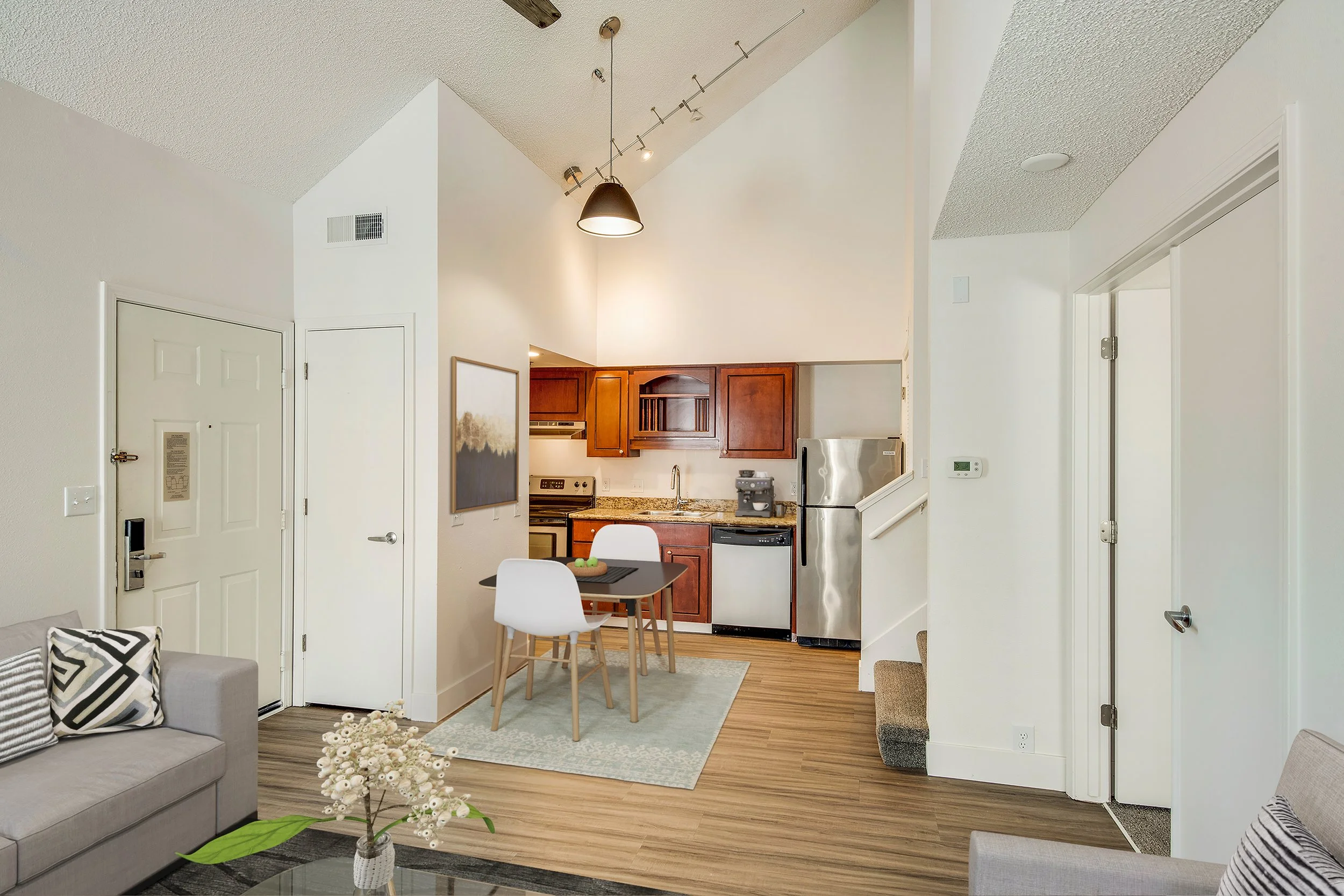 Interior of a modern apartment with a view of the living room, dining area, and kitchen. White walls, wooden floors, contemporary furniture, and kitchen appliances.