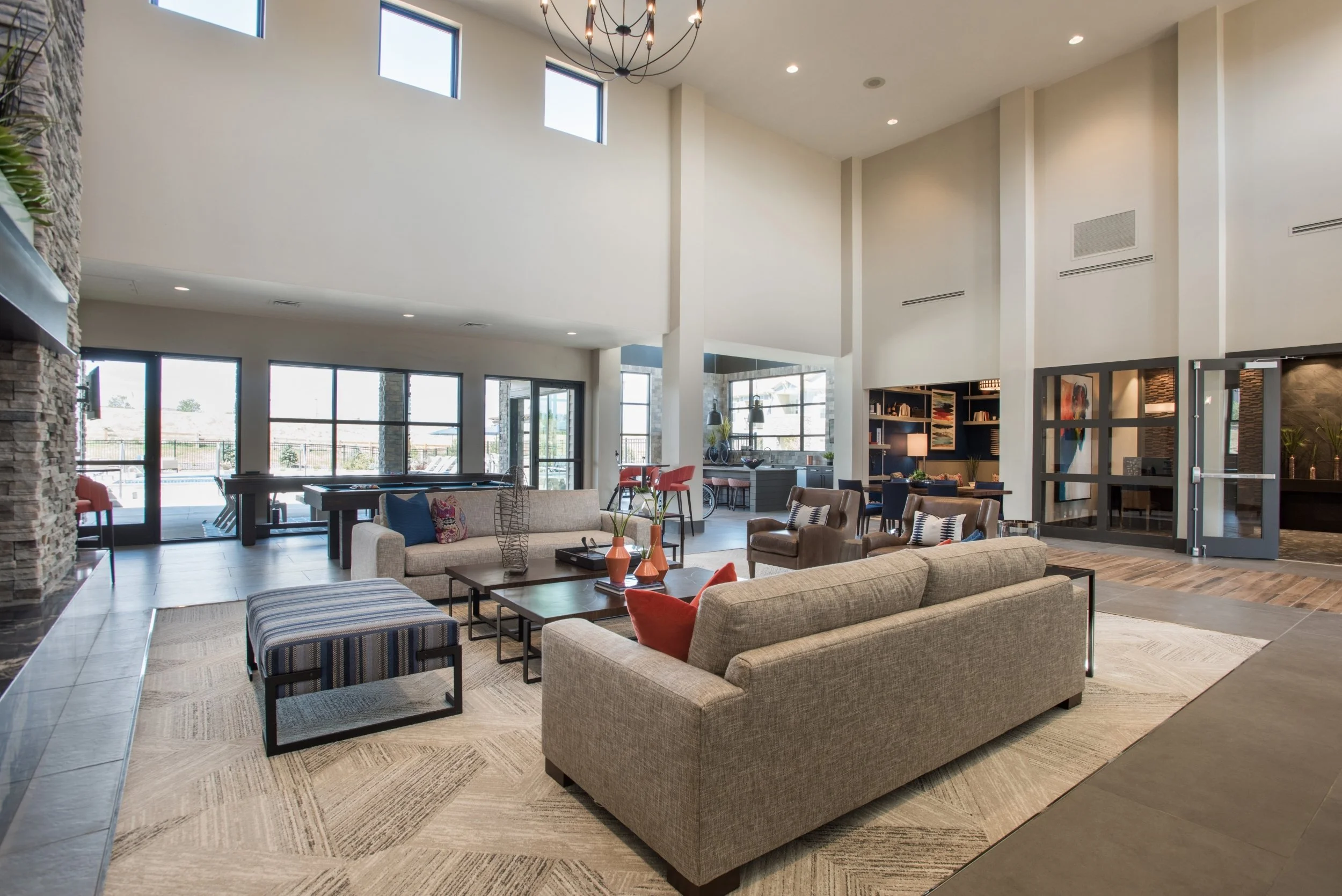Spacious modern living room with high ceilings, large windows, and contemporary furniture, including sofas, armchairs, a coffee table, and decorative vases.
