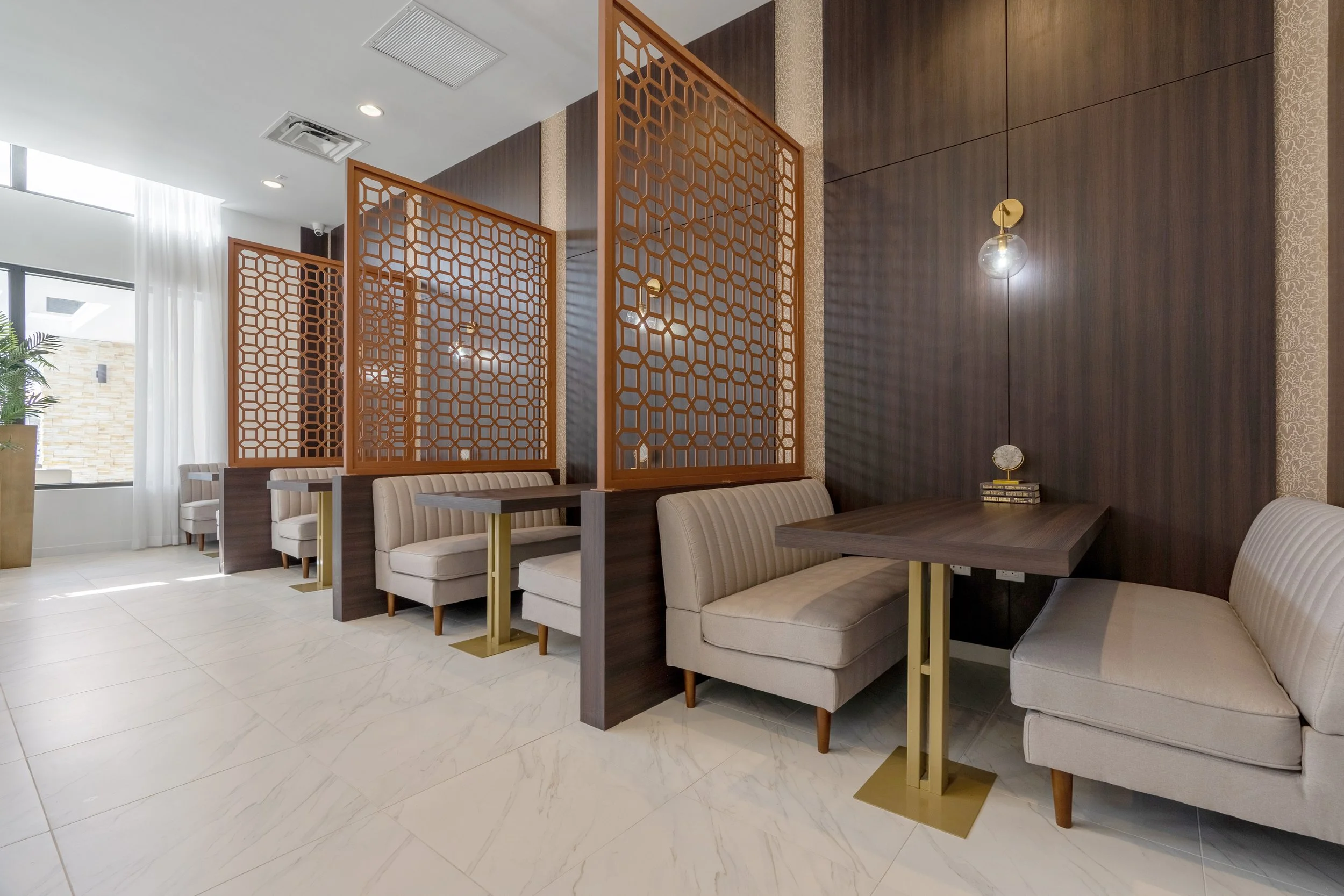 A modern interior with cozy booths separated by wooden lattice dividers, beige cushioned seats, dark wood tables, and wall-mounted decorative lighting fixtures.