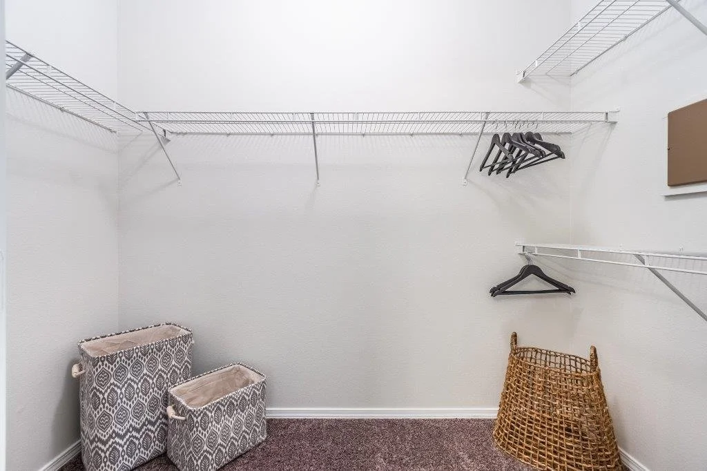 Empty closet with white wire shelving, black hangers, woven basket, and fabric storage bins.