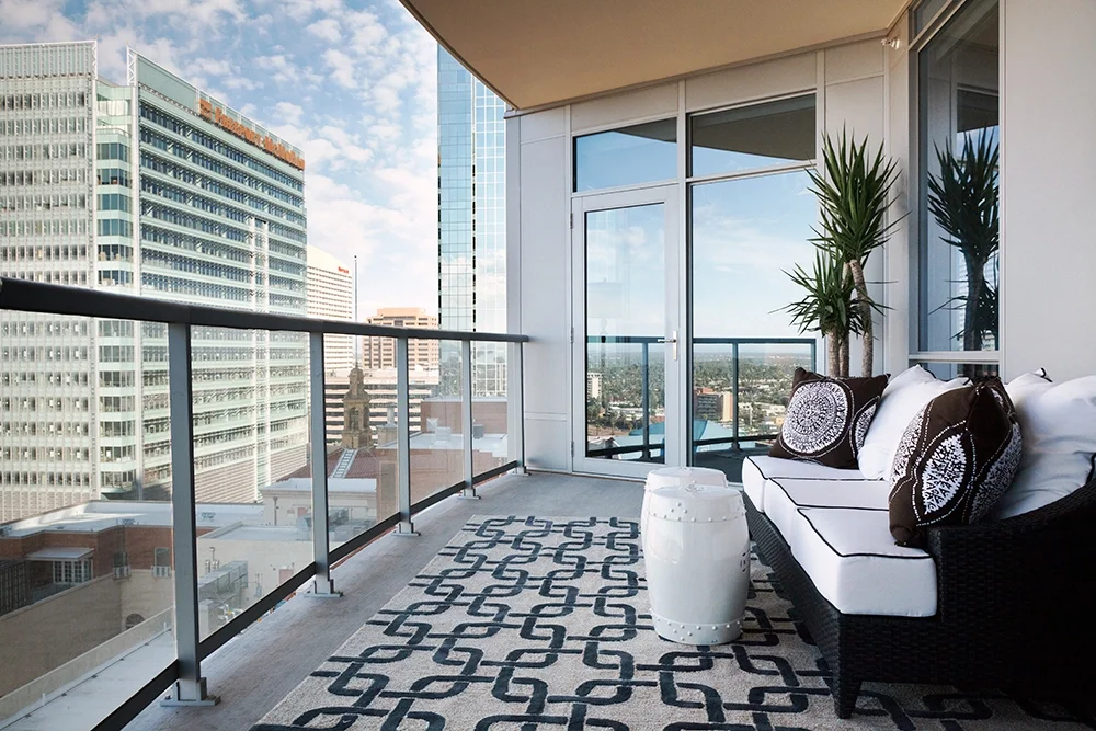 Balcony with black and white furniture, patterned rug, potted plant, view of tall buildings and cityscape.