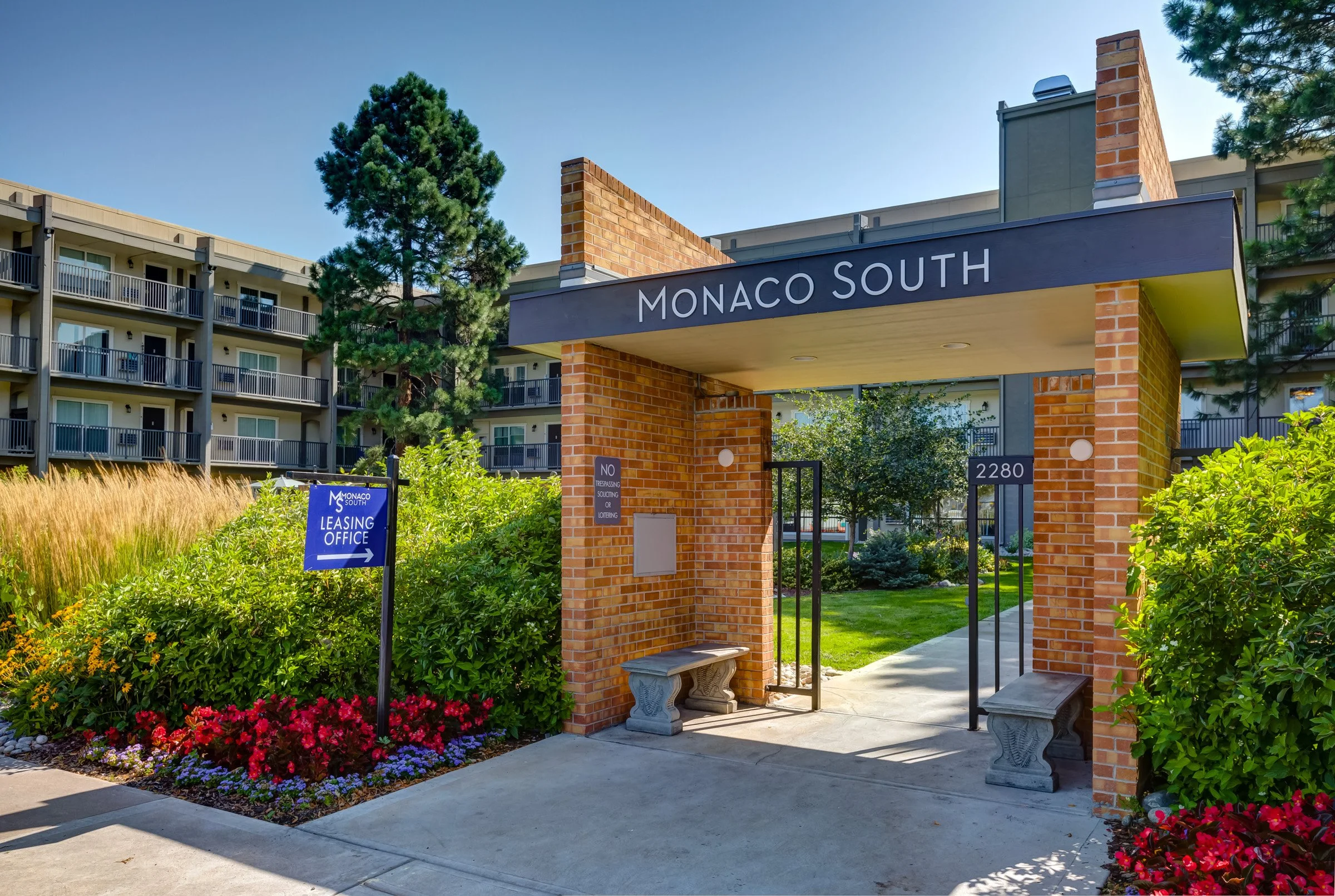 Entrance to Monaco South apartment complex with a brick archway, sign, landscaping, and a nearby building with balconies.