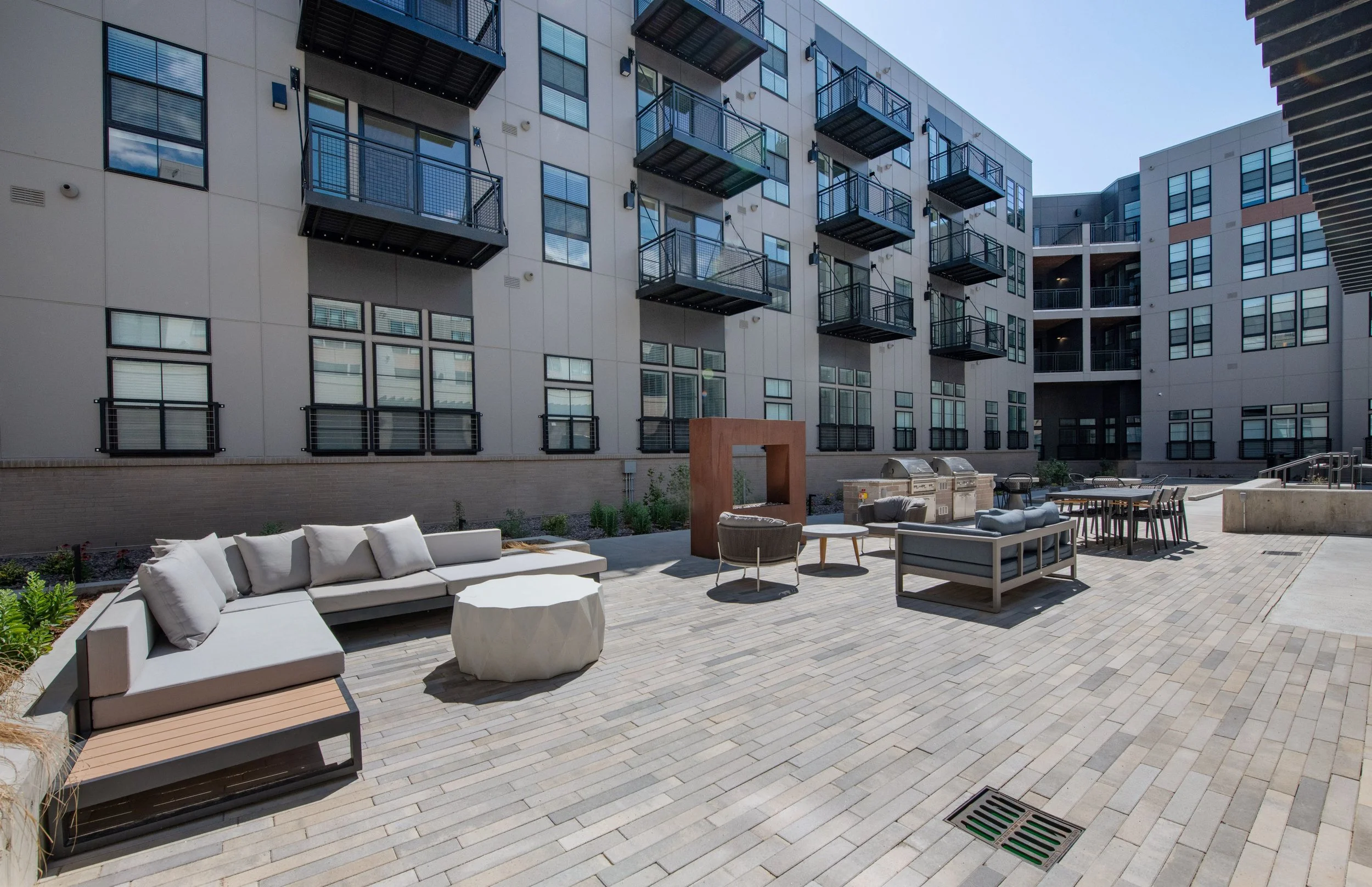 Apartment complex courtyard with outdoor seating, lounge chairs, tables, and buildings with balconies.