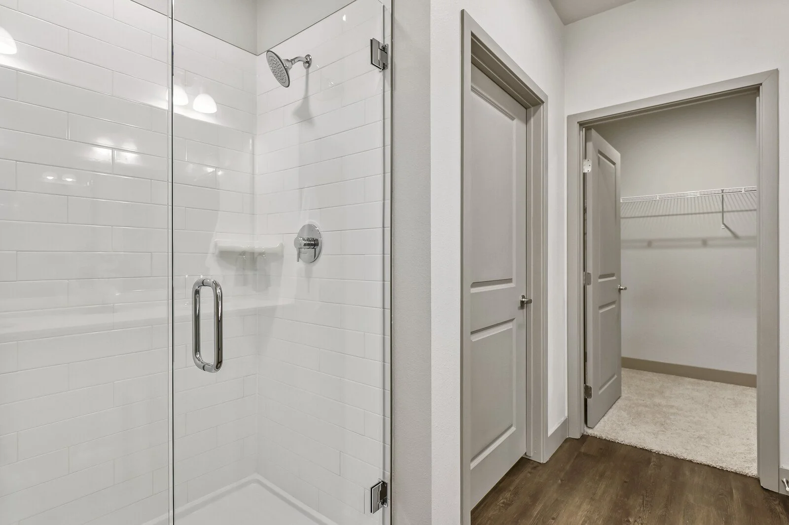 Inside a bathroom with a glass-enclosed shower on the left and a walk-in closet with wire shelves on the right.