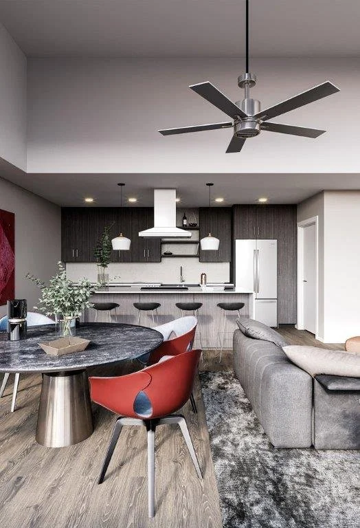 Modern open-concept living room and kitchen with gray and black color scheme, round dining table with red chairs, gray sectional sofa, ceiling fan, and pendant lighting over the kitchen island.