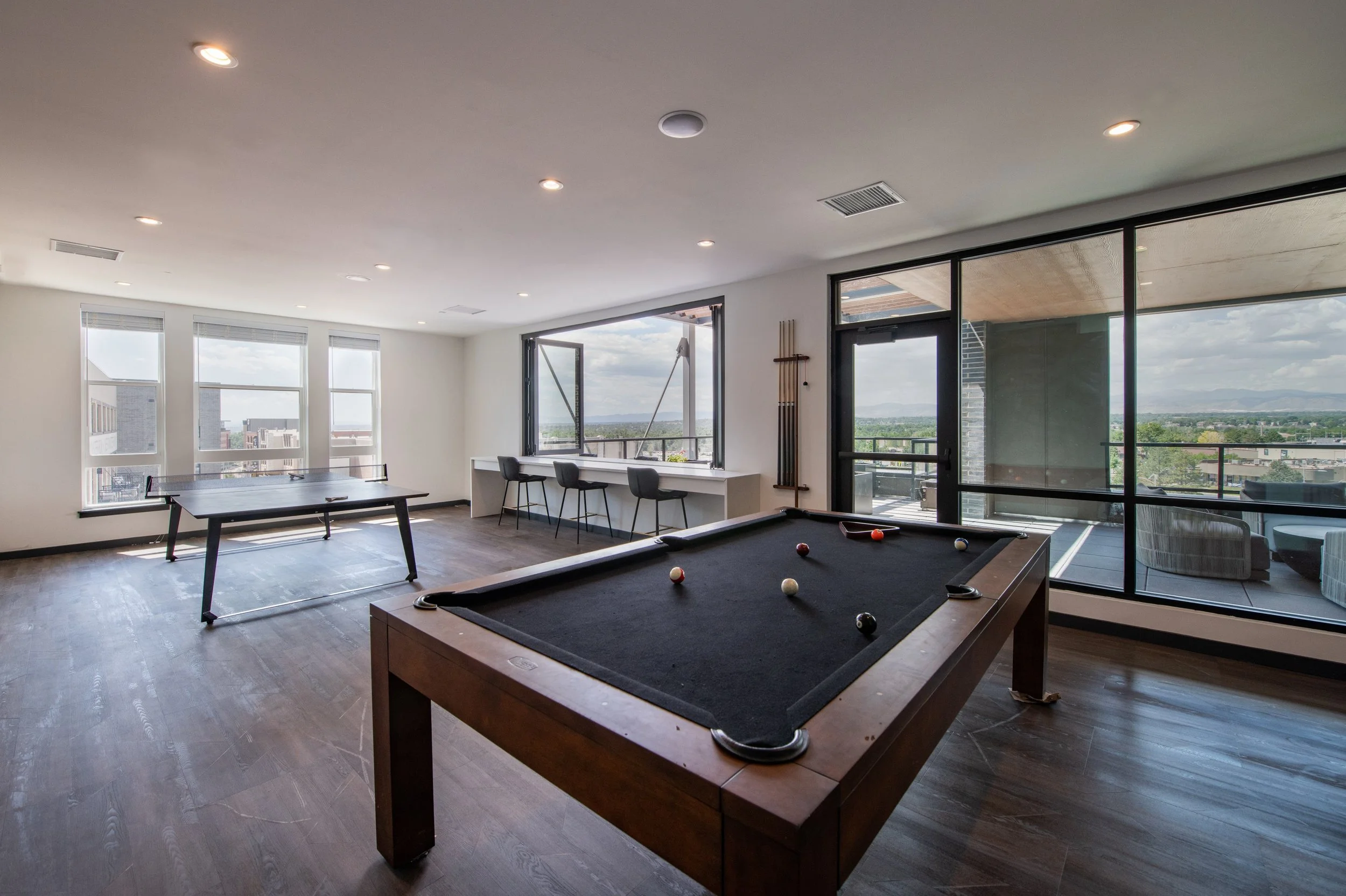 Indoor recreational room with billiards table, table tennis, window seats, balcony, and city view.