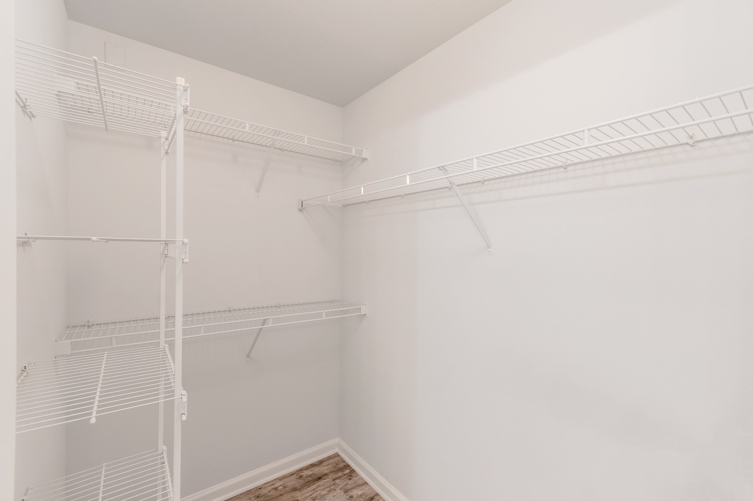 Empty white walk-in closet with wire shelves on white walls and wood laminate flooring.