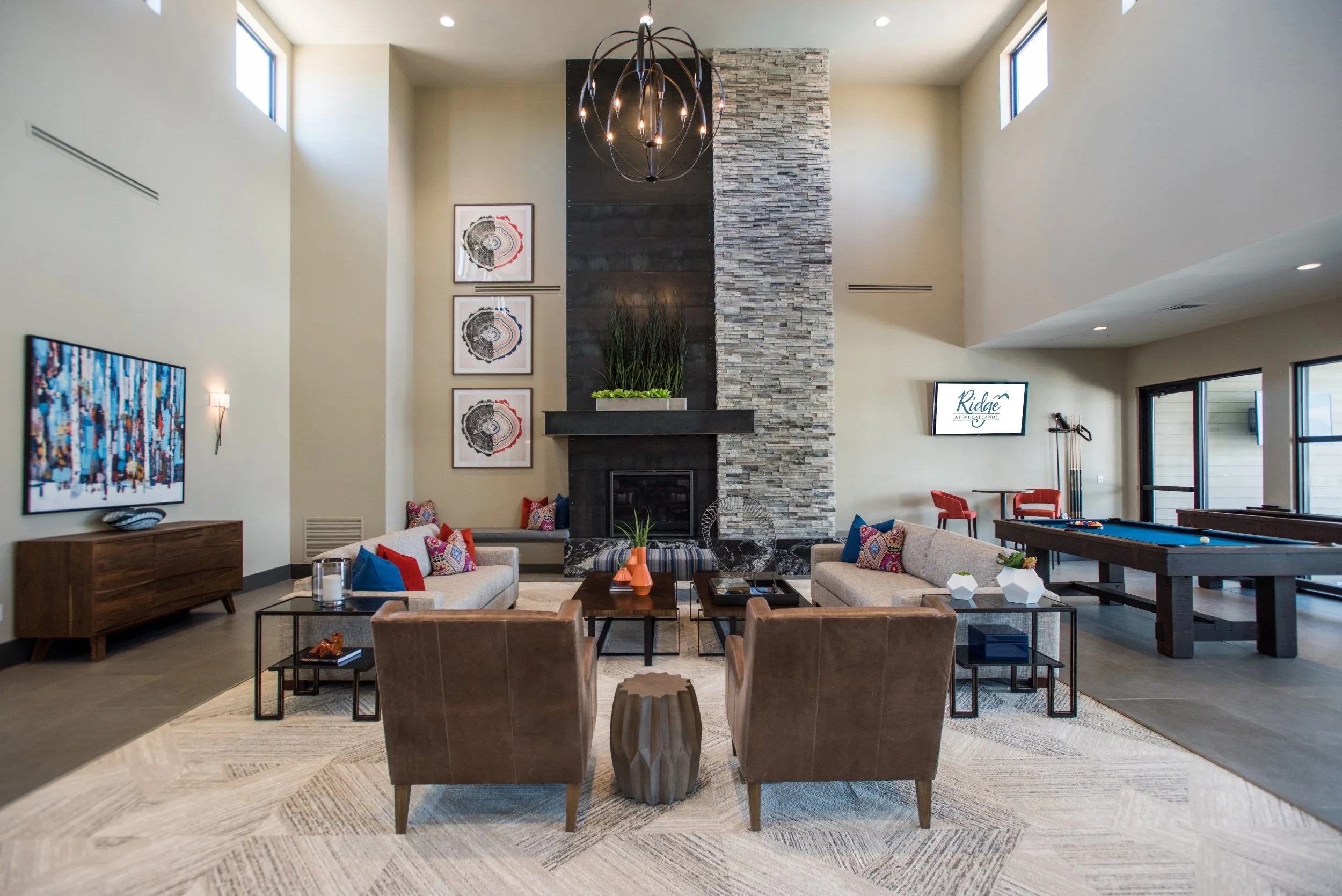 Modern living room with high ceiling, stone fireplace, contemporary furniture, and large windows.