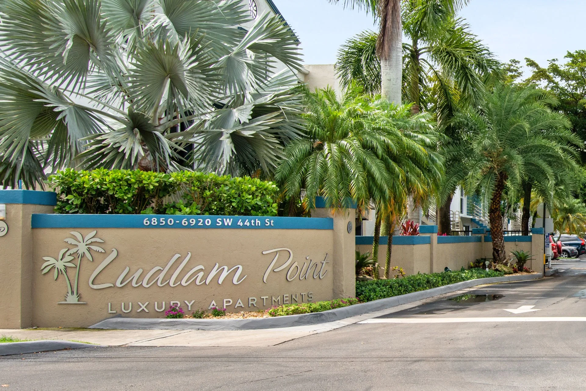 Entrance sign for Ludlam Point luxury apartments with palm trees and greenery