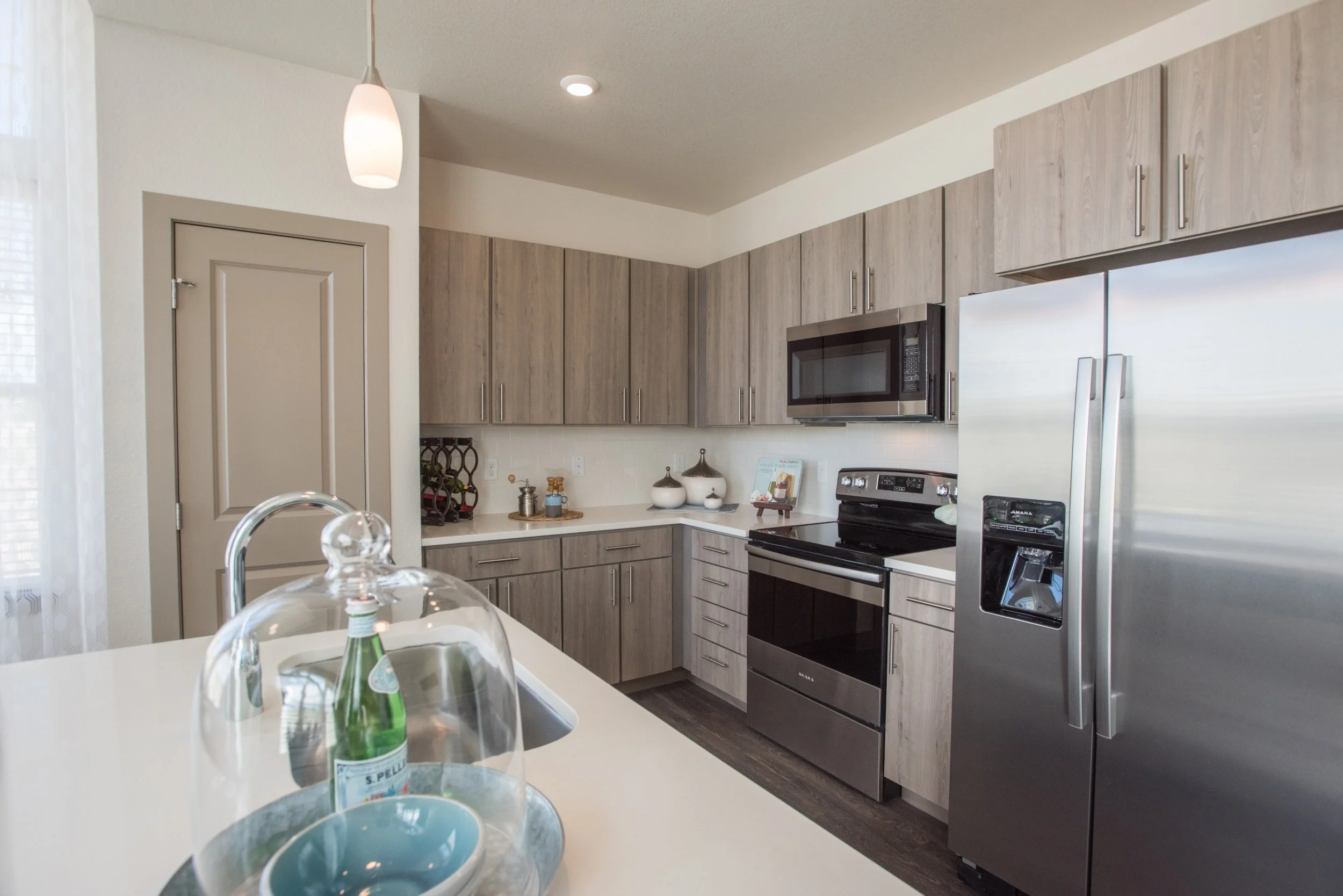 Modern kitchen with gray wood cabinets, stainless steel appliances including a refrigerator and oven, black microwave, and countertop decor with bowls and small decorative items.