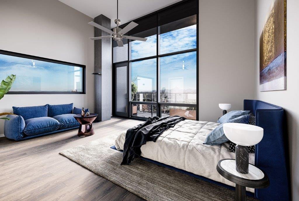 Modern bedroom with large floor-to-ceiling windows, a blue velvet bed, two white nightstands with lamps, a beige rug, and a blue sofa with a wooden side table.