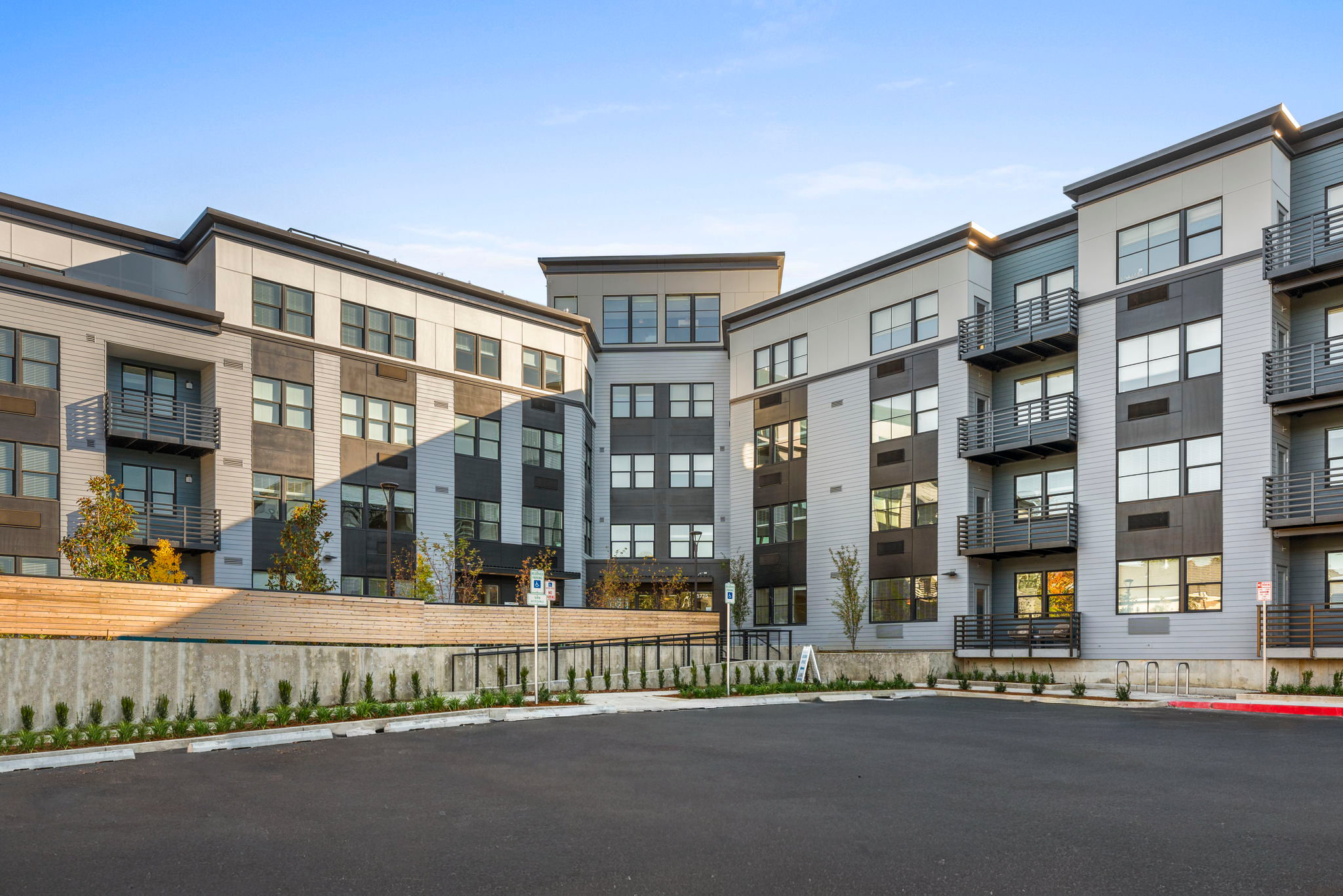 Modern multi-story residential apartment building with balconies, large windows, and a landscaped courtyard in the foreground.