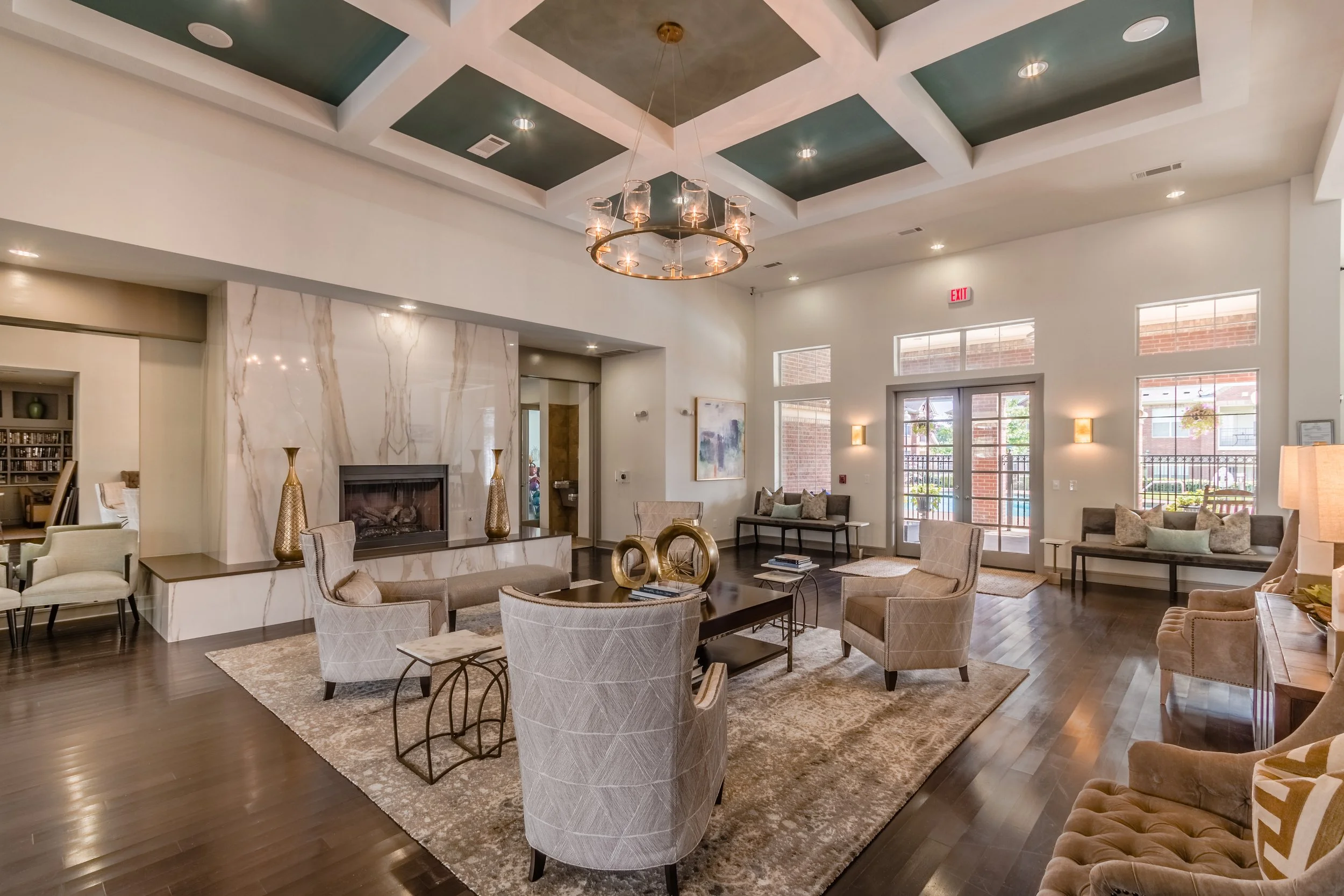Spacious, modern lobby with high ceiling, chandelier, fireplace, seating area with armchairs and benches, large windows, and wood flooring.