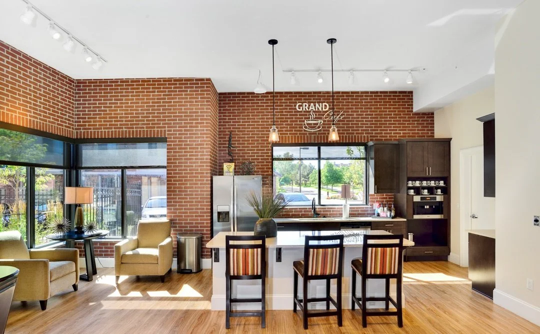 Modern kitchen and living area with brick walls, large windows, a kitchen island with bar stools, and seating area with chairs and a lamp.