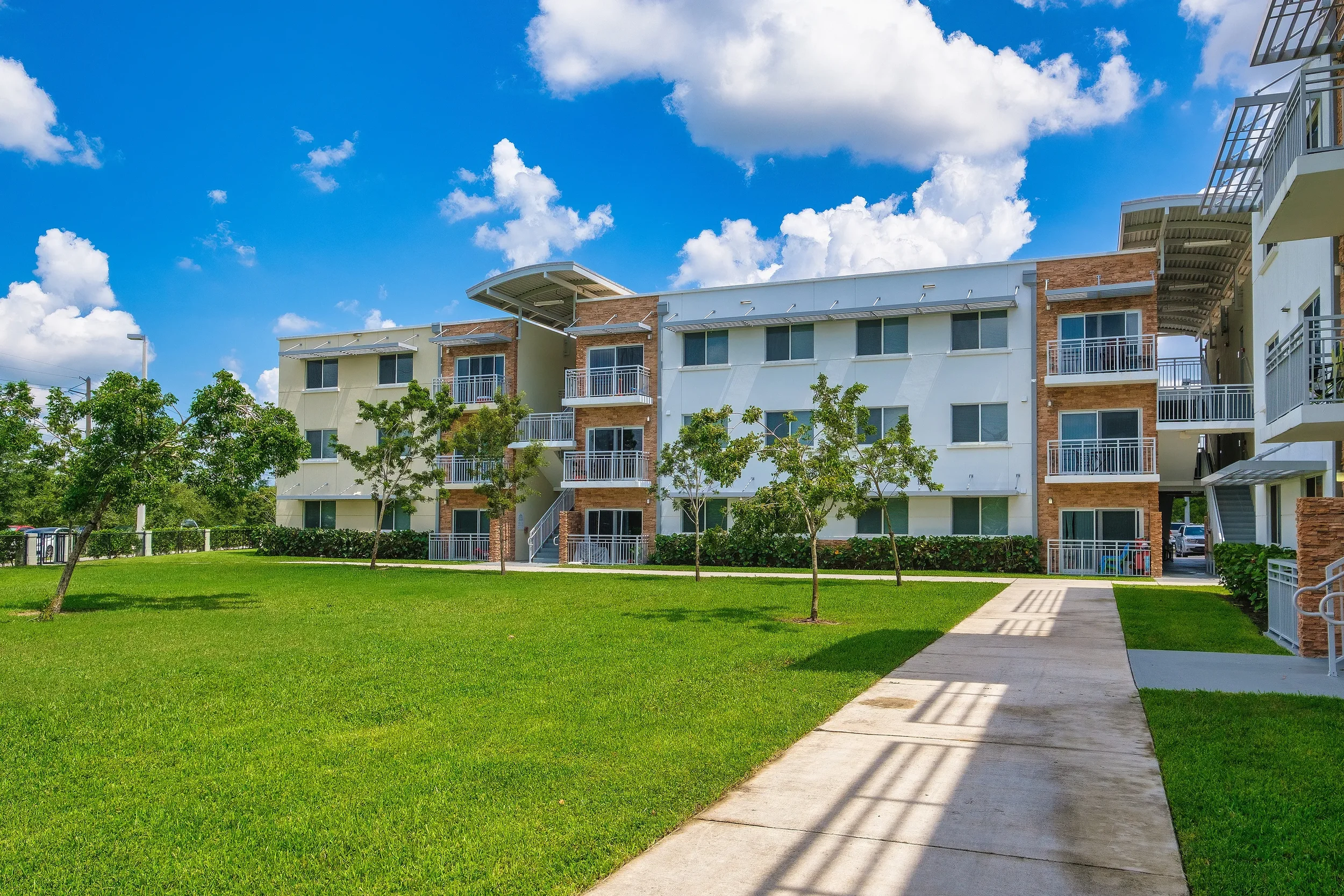Luxury apartment complex under a blue sky with white clouds with a foreground of lush green lawn.