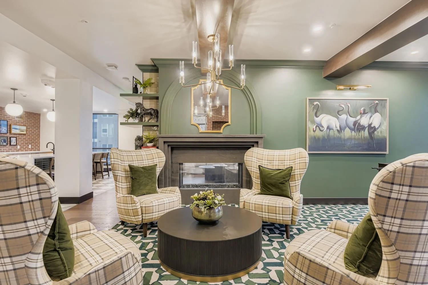 Living room with armchairs, green pillows, fireplace, art painting of flamingos, chandelier, and decorative plants.