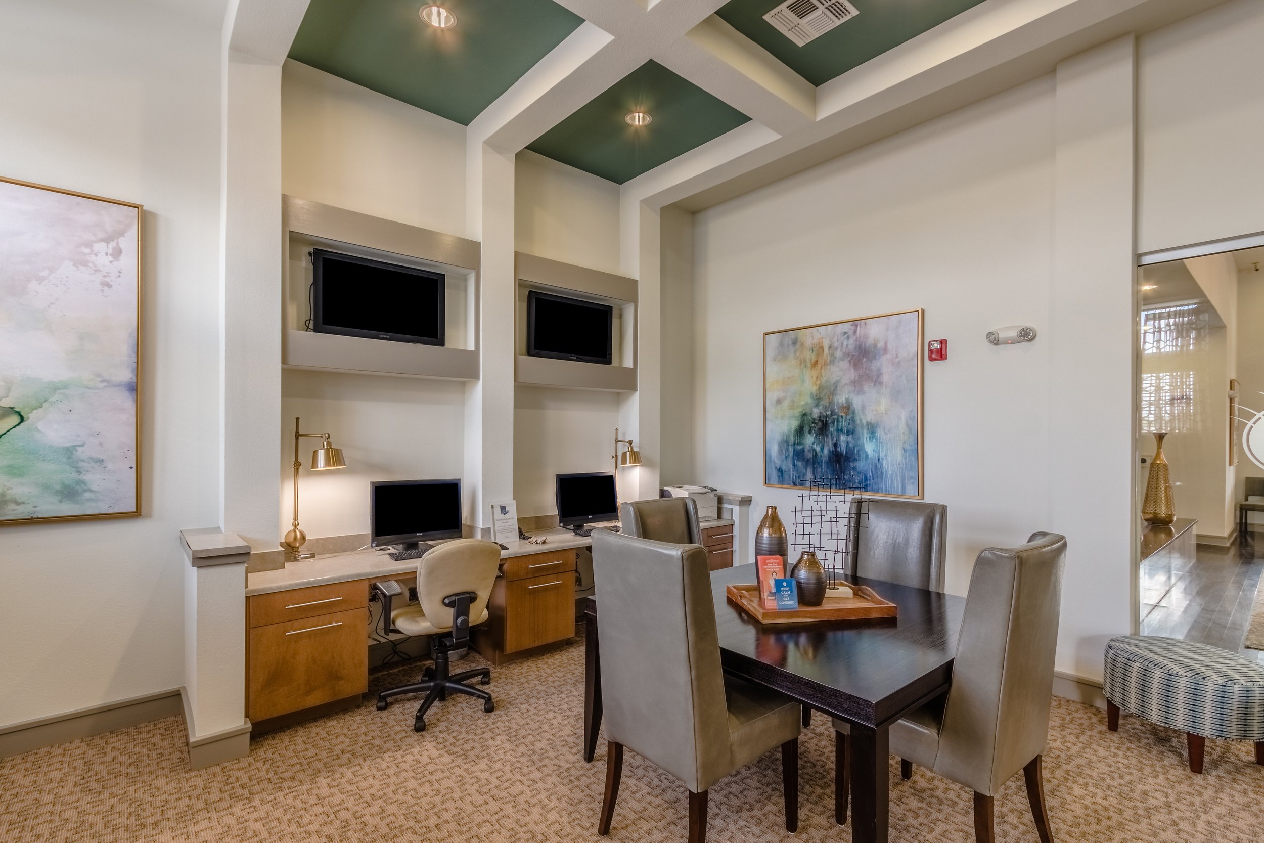 Hotel lobby area with a desk, chairs, artwork, and multiple monitors on the wall.