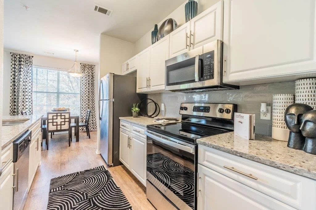 Kitchen with white cabinets, stainless steel appliances, granite countertops, and a dining area with a window and patterned curtains.