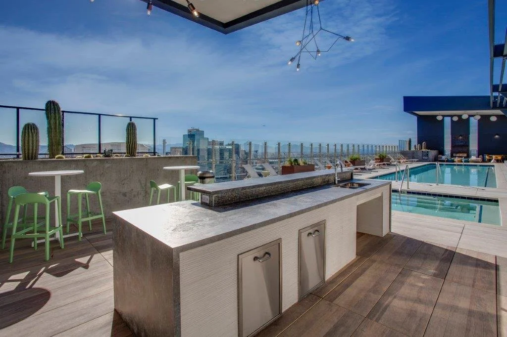 Rooftop pool area with city skyline view, pool, outdoor seating, and cactus plants.