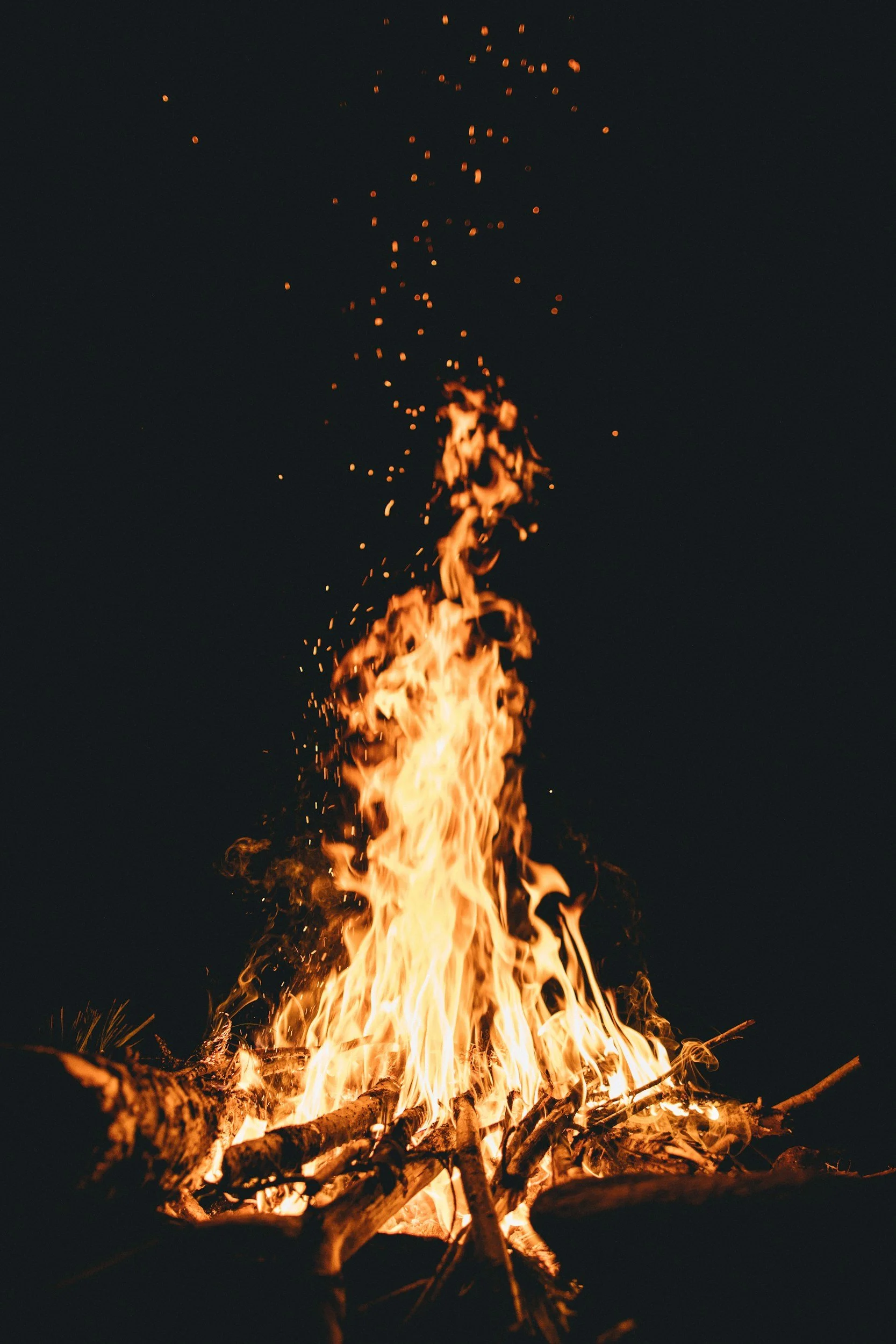 A campfire made of logs burning with tall flames against a dark night sky.