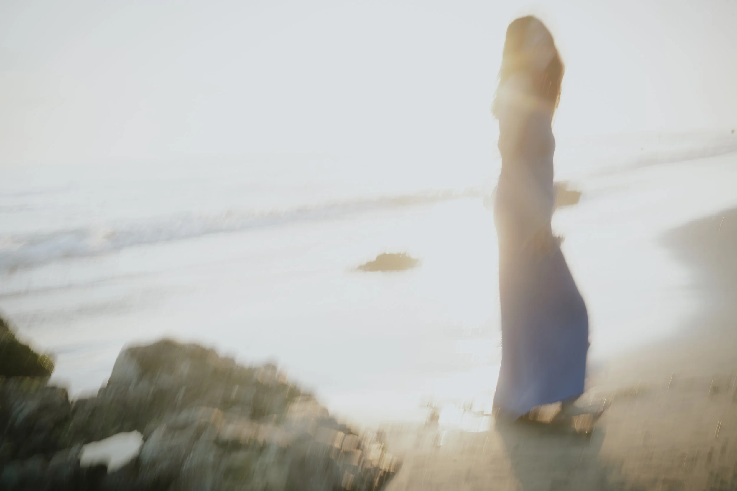 A person standing on a beach during sunset, with the sun shining brightly behind them, creating a silhouette effect.