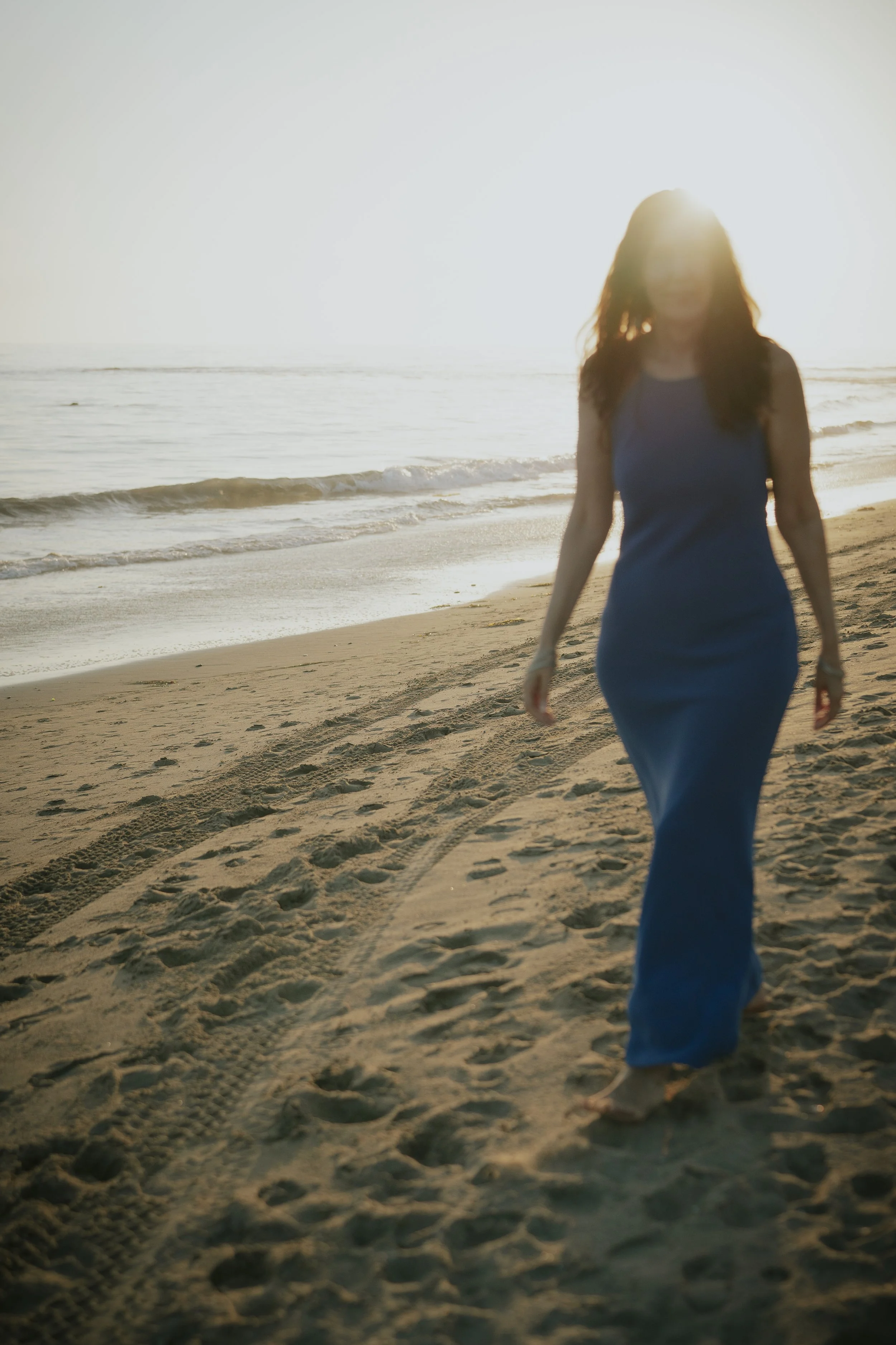 Woman walking on the beach at sunset in a blue dress.