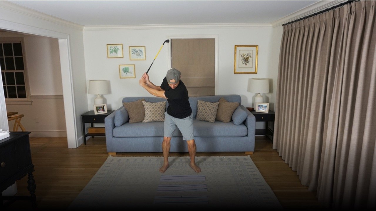 Adam Kolloff practicing golf swings indoors in a living room.