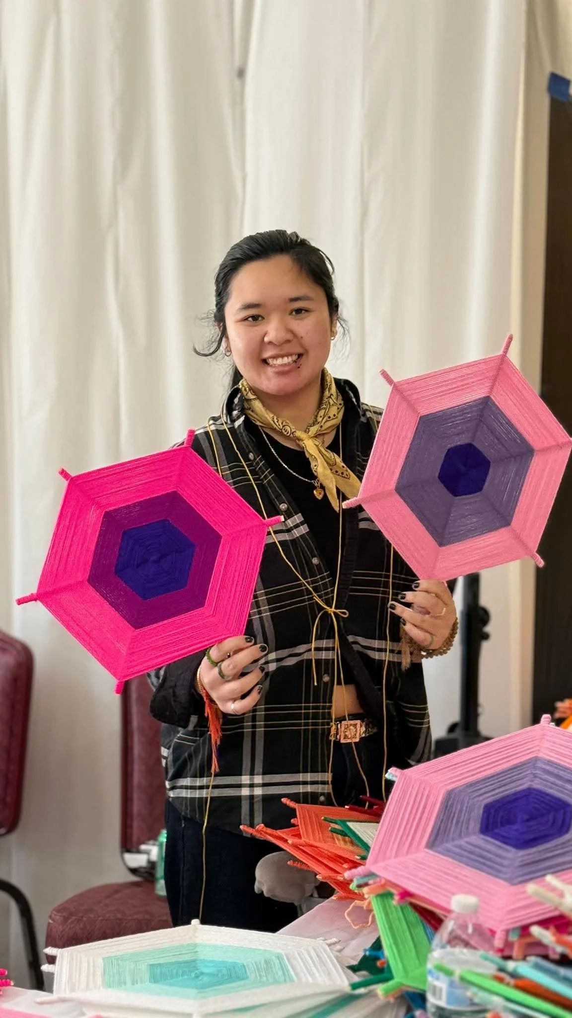 A young woman smiling and holding decorated pink and purple paper lanterns at a table filled with more lanterns.
