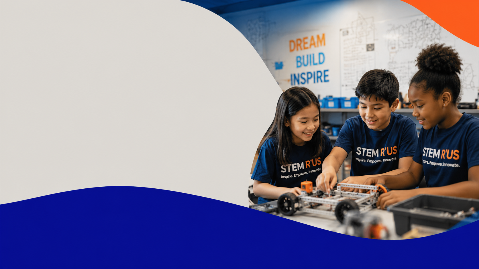 Three children working on a robotics project at STEM R'US, wearing matching blue shirts, smiling and collaborating in a classroom with posters that say 'Dream, Build, Inspire' in the background.