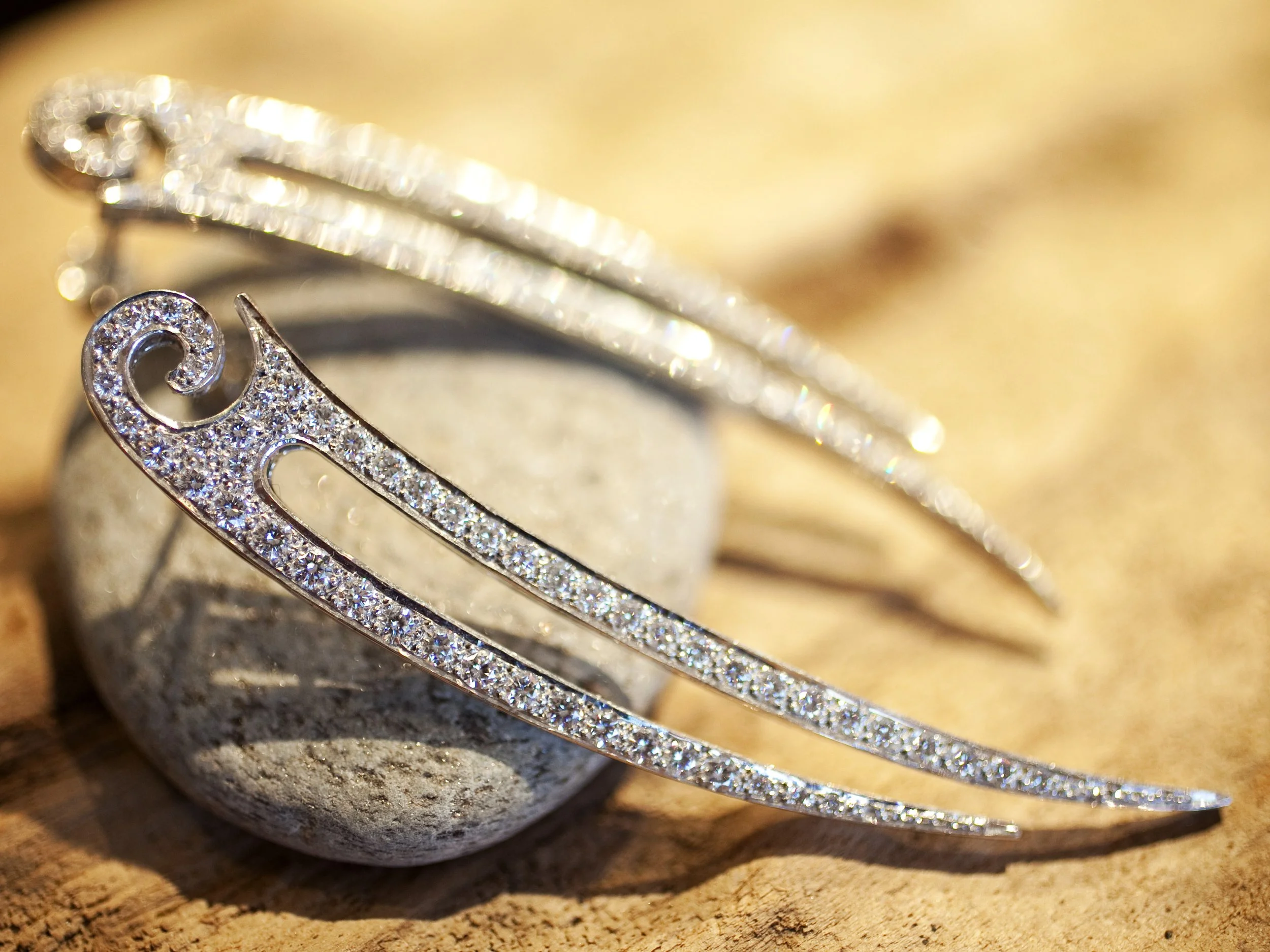 Close-up of a silver, rhinestone-studded hairpin resting on a small, smooth rock on a wooden surface.