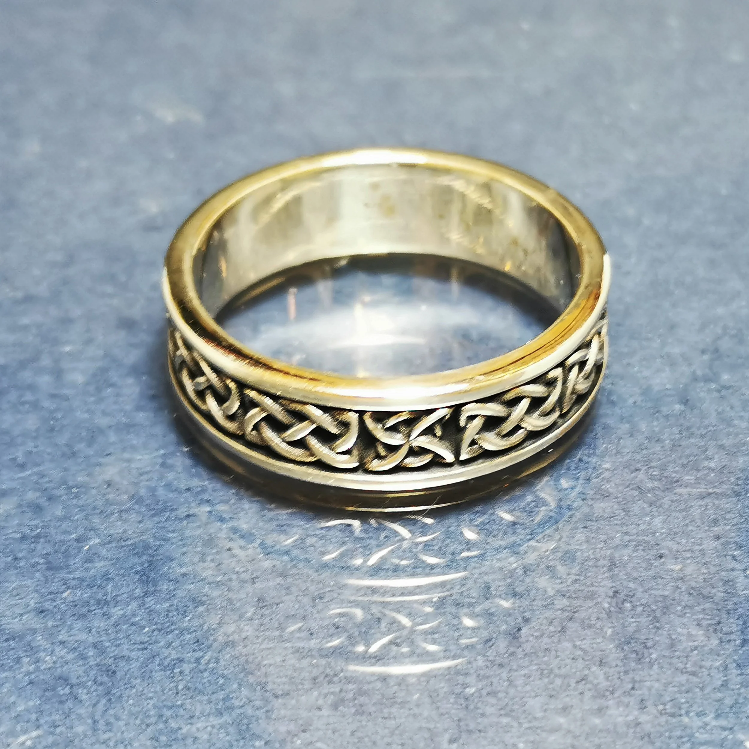 A silver ring with intricate Celtic knotwork design on top, placed on a gray surface.