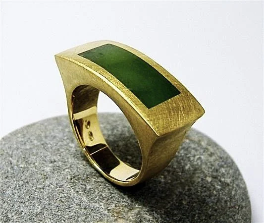Gold ring with a rectangular green stone, resting on a gray stone surface.