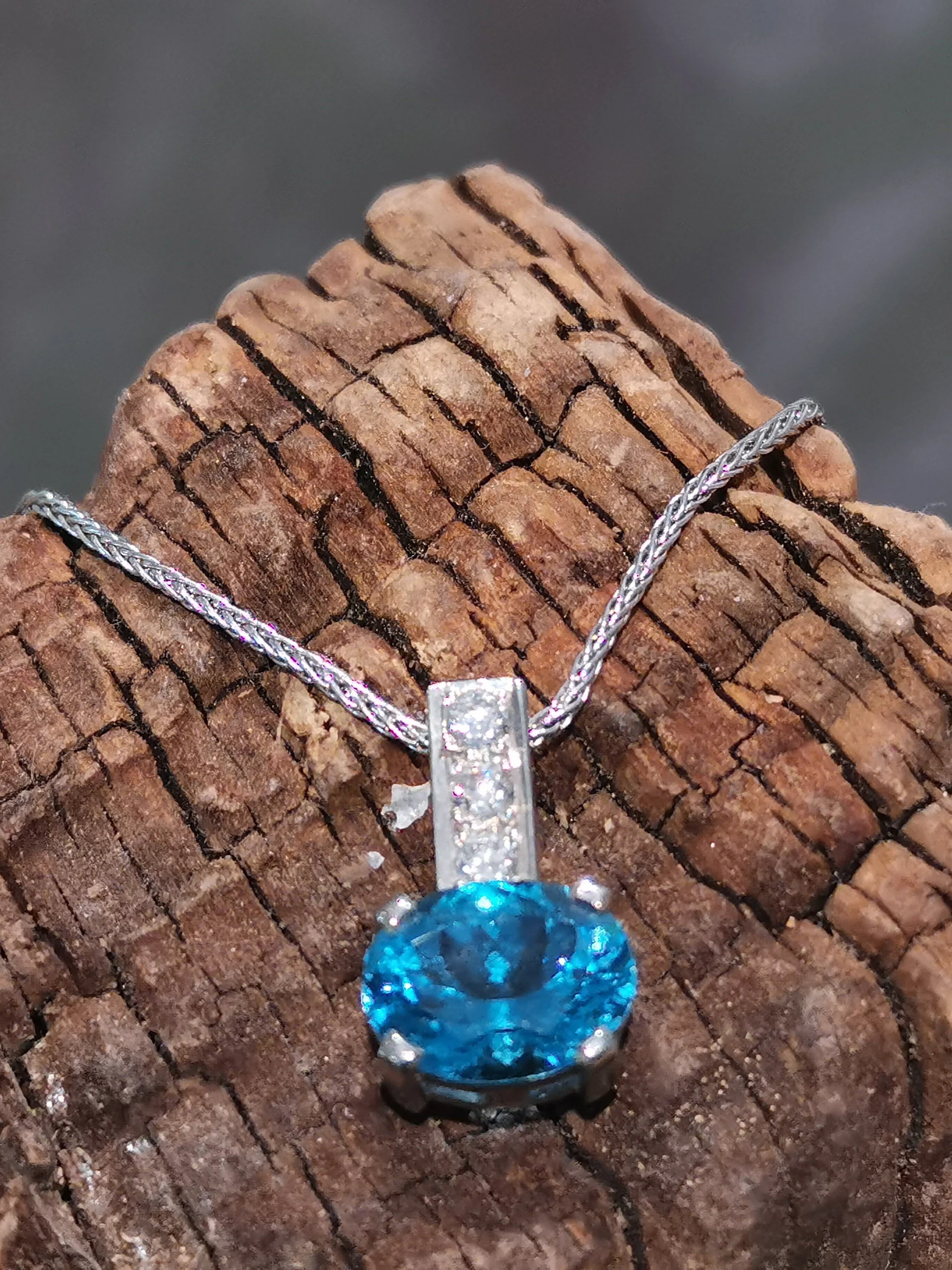 Silver necklace with a large blue gemstone pendant displayed on a textured wooden surface.