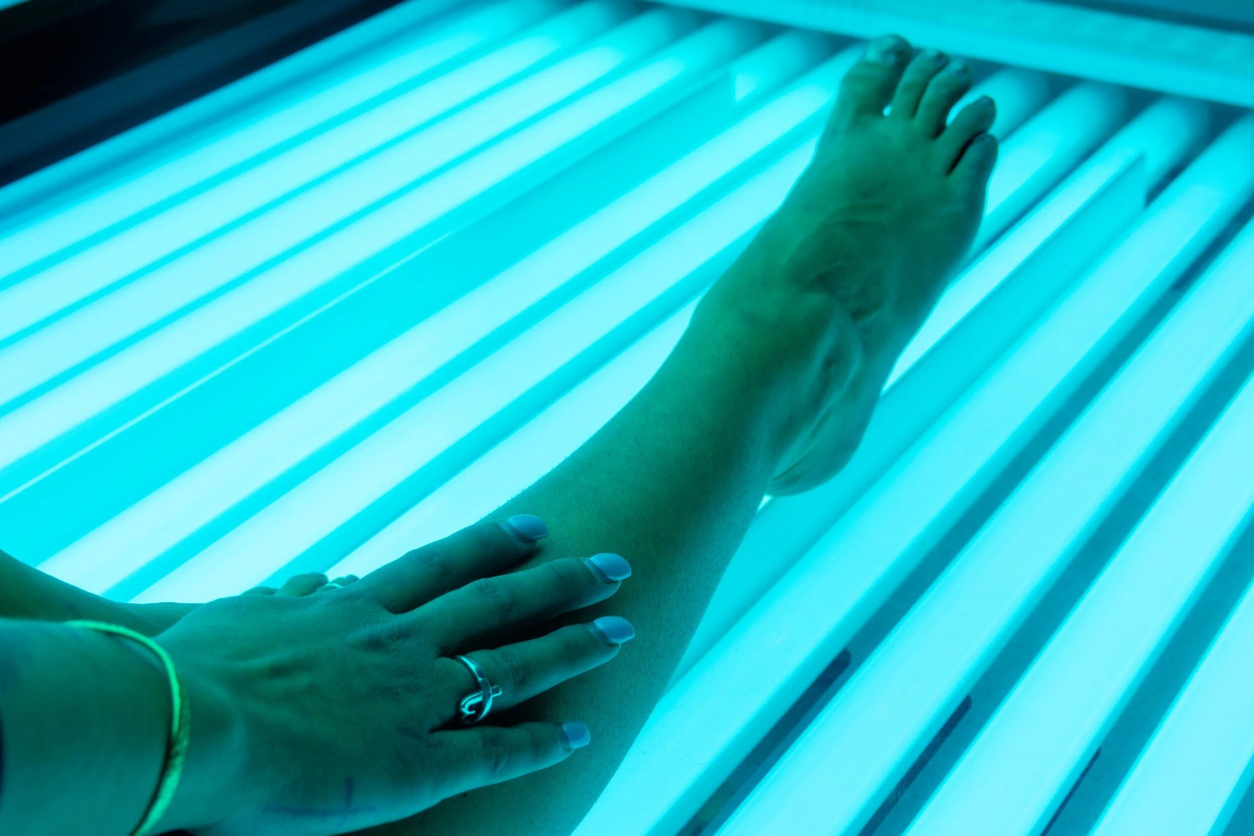 A person's hand and arm resting on a glowing blue light panel, with fingers slightly spread apart, in a dark room.