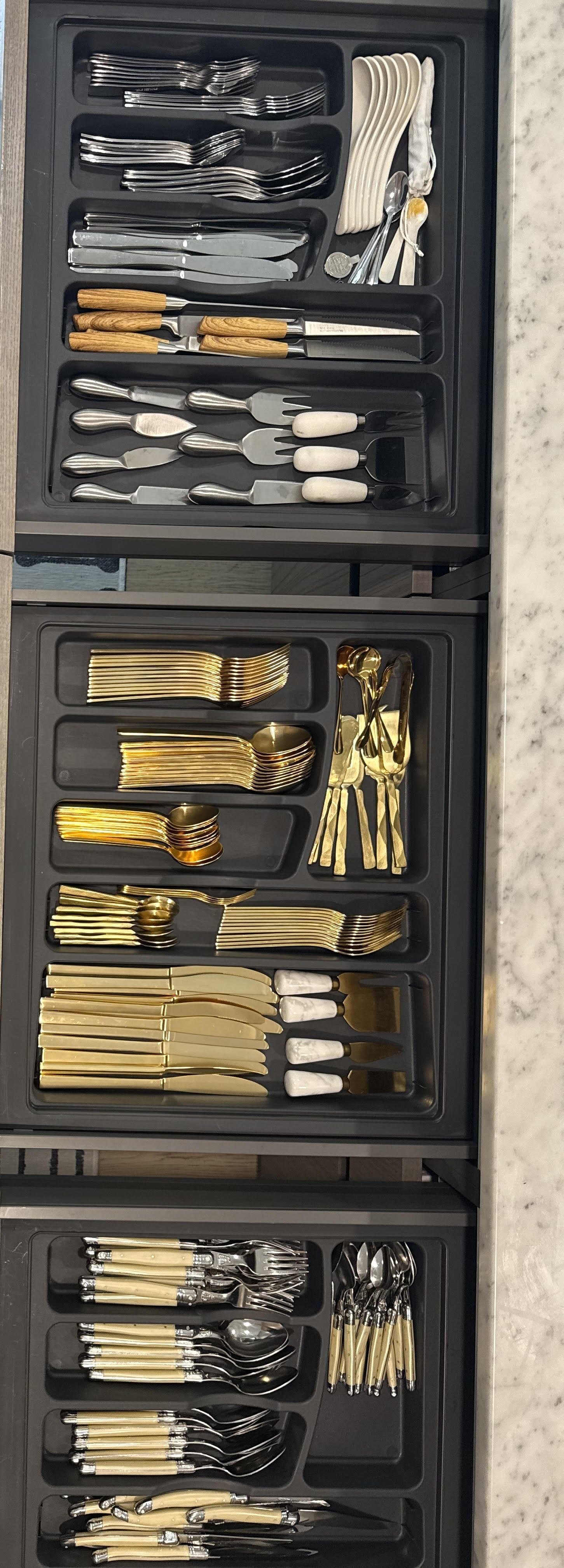 Set of organized silverware and utensils including forks, knives, spoons, dessert forks, teaspoons, and serving utensils arranged in black trays.