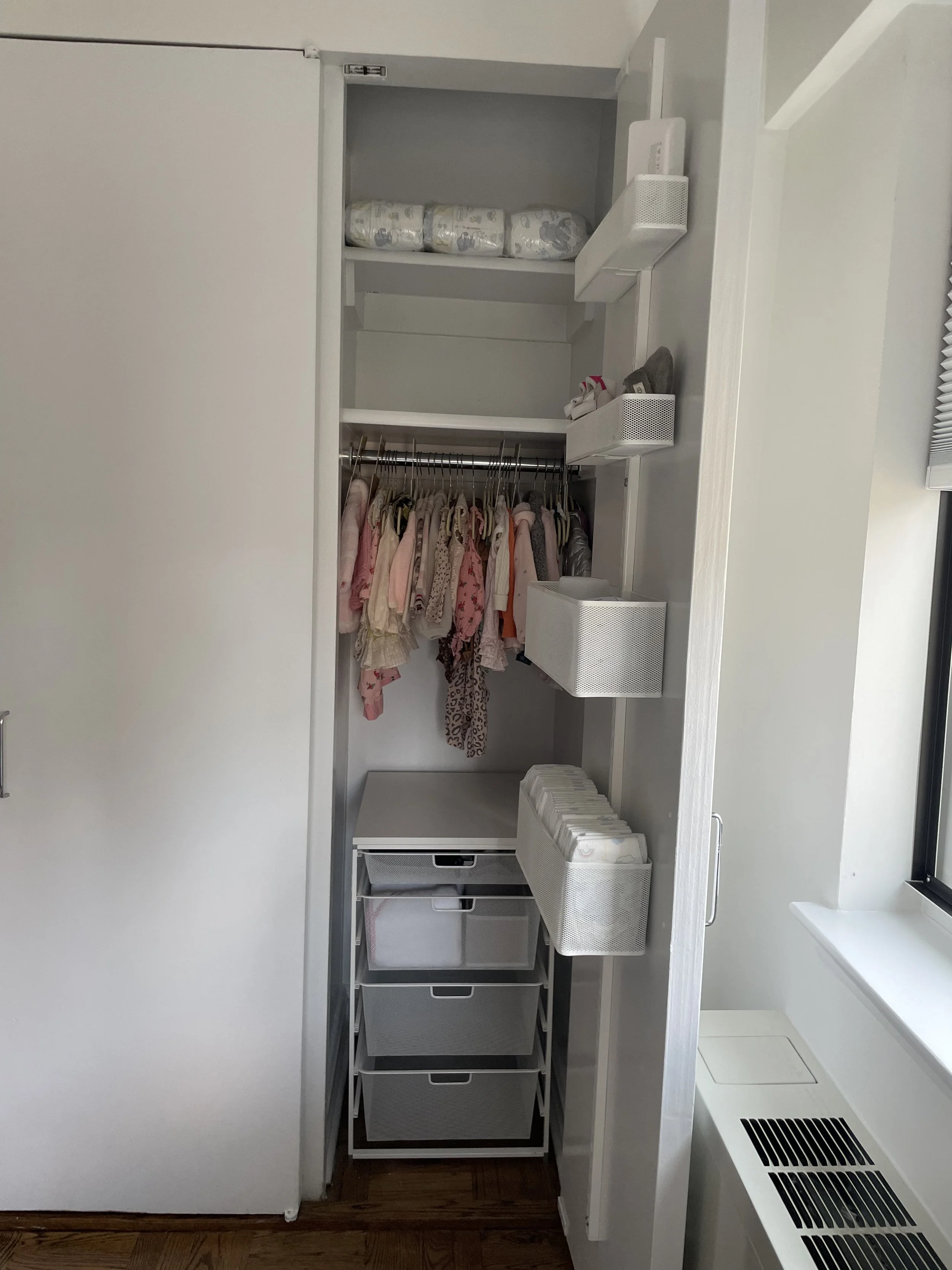 Closet with white drawers, shelves, hanging clothes for kids, and storage boxes.