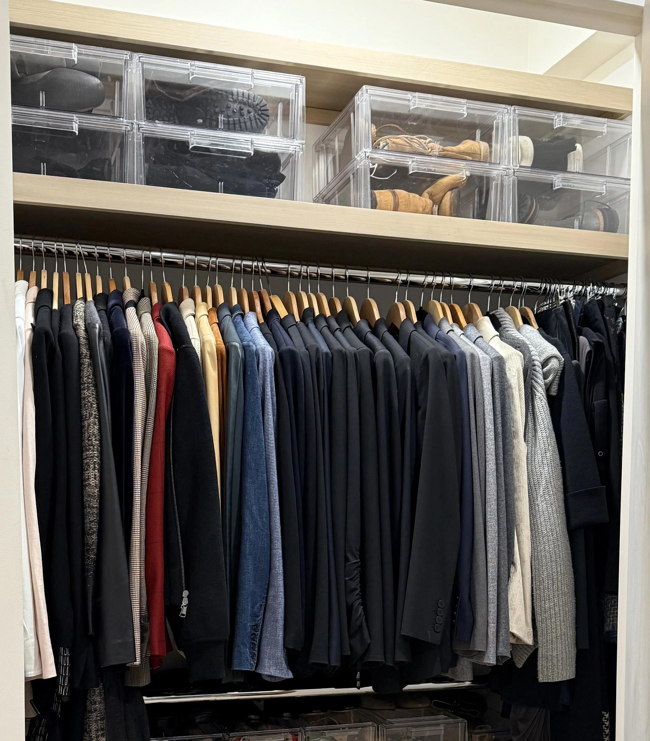Closet with hanging men's clothing, including jackets, blazers, and sweaters, and organized shoe boxes on upper shelves.