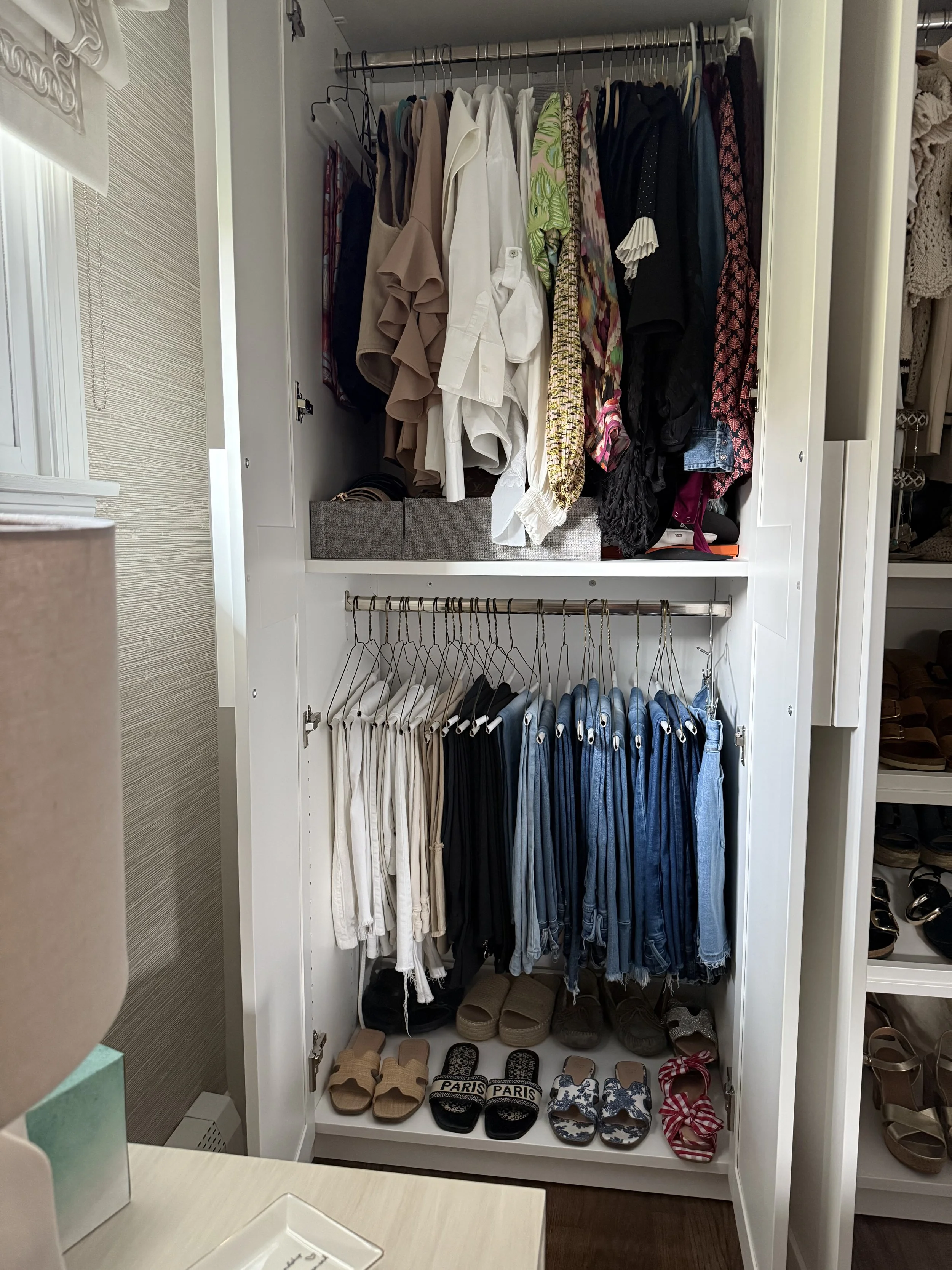 Open wardrobe with neatly arranged clothes on top and bottom, and sandals and slippers on the floor.