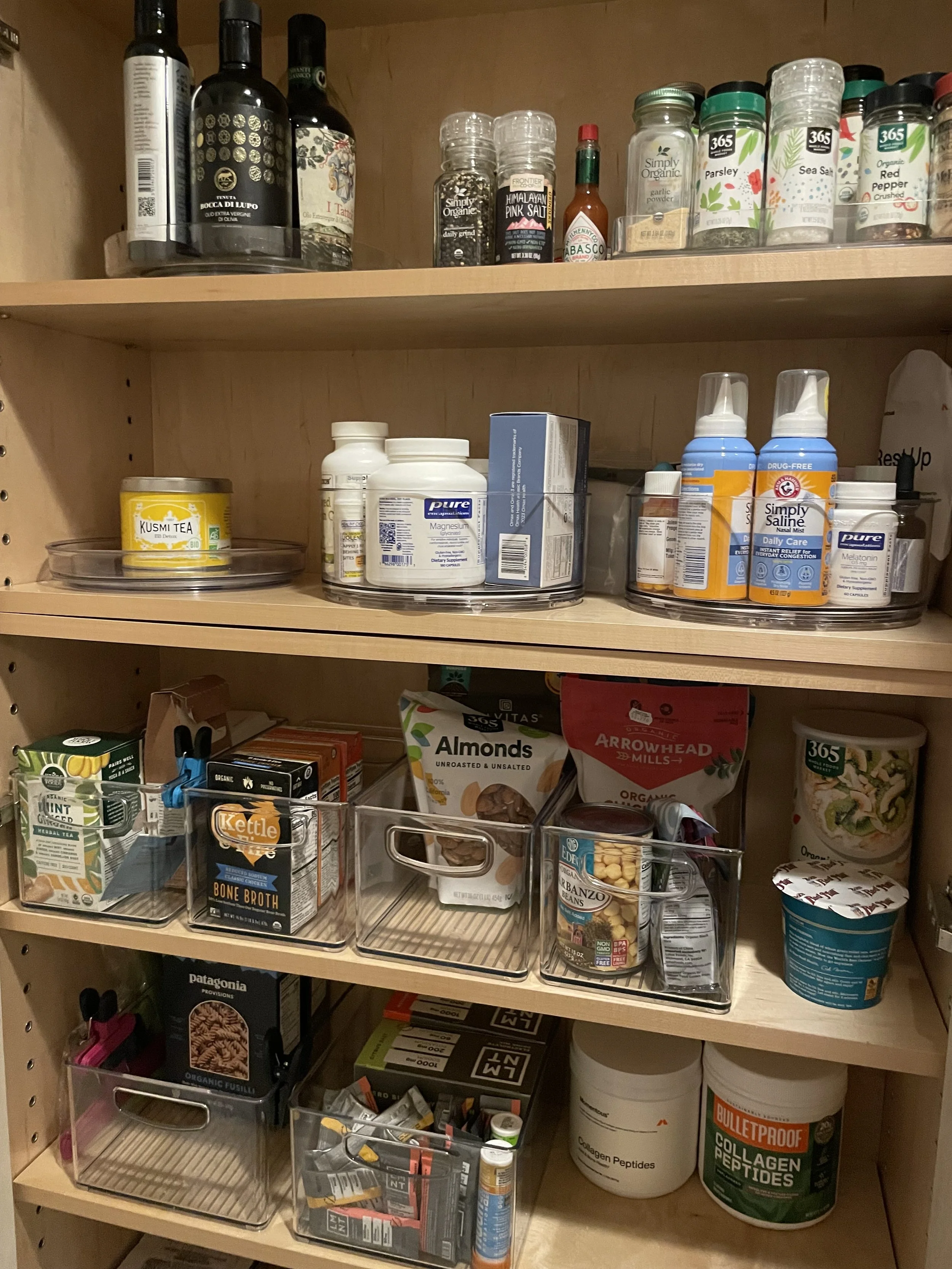 A wooden pantry shelf filled with bottles, jars, dietary supplements, and food items.