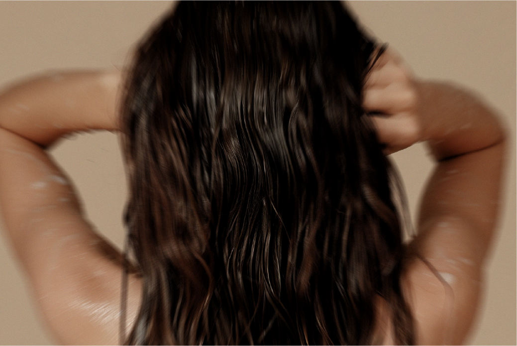 Person with wet, dark brown hair from behind, arms raised.