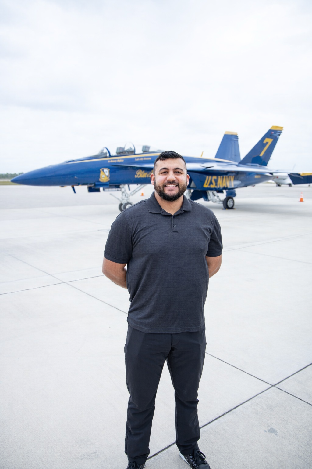 Man standing on tarmac with U.S. Navy fighter jet in background.